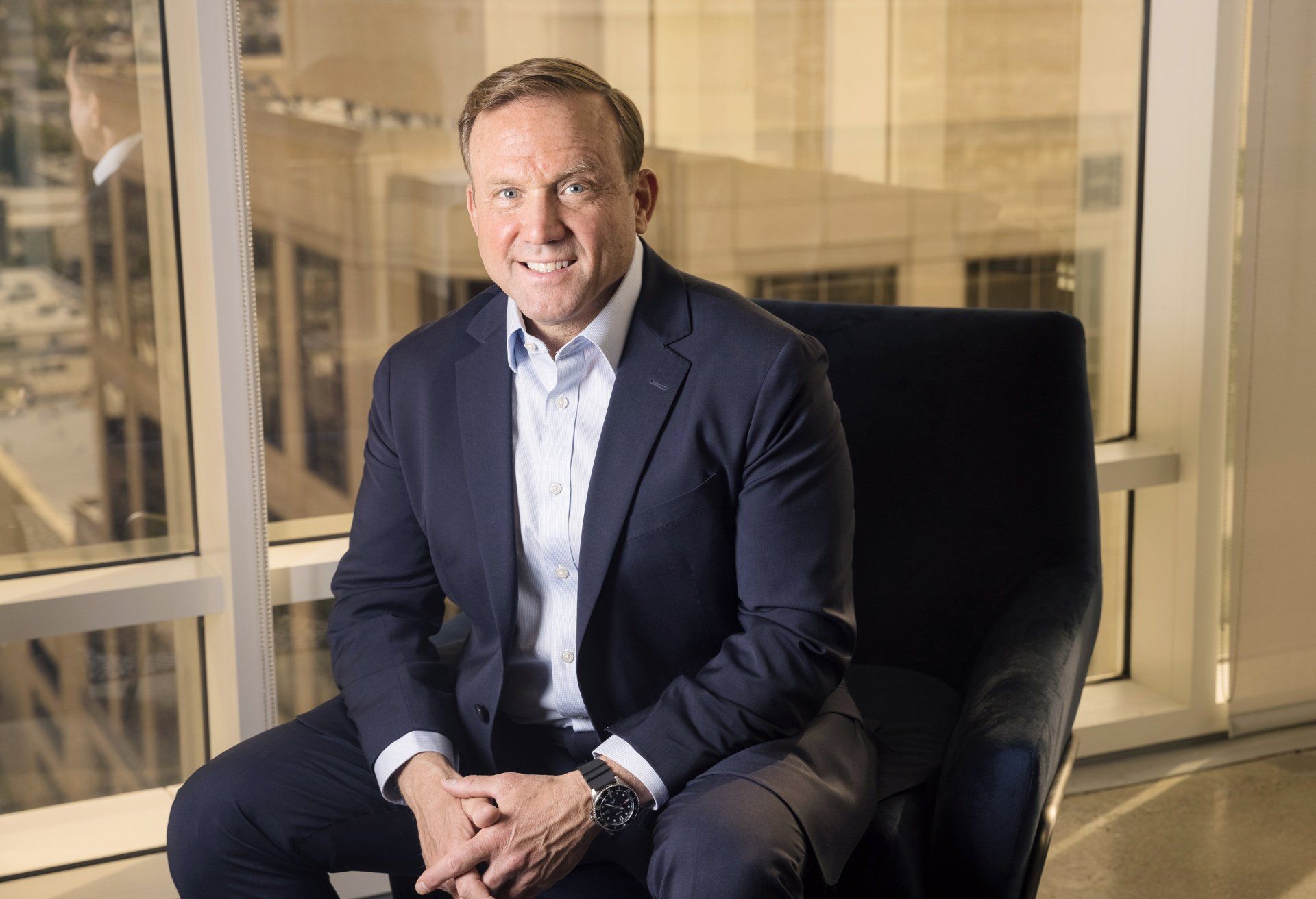 A man in a suit is sitting in a chair in front of a window.