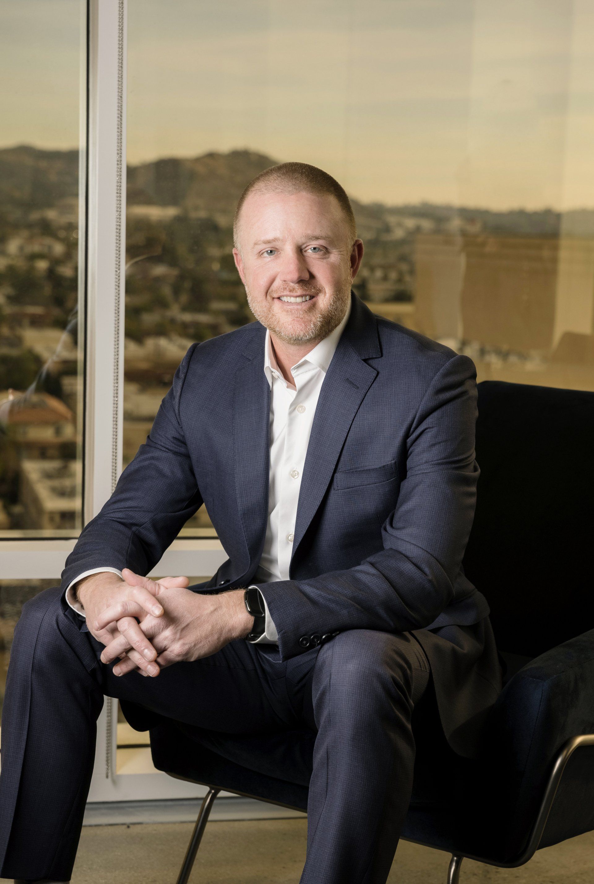 A man in a suit is sitting in a chair in front of a window.