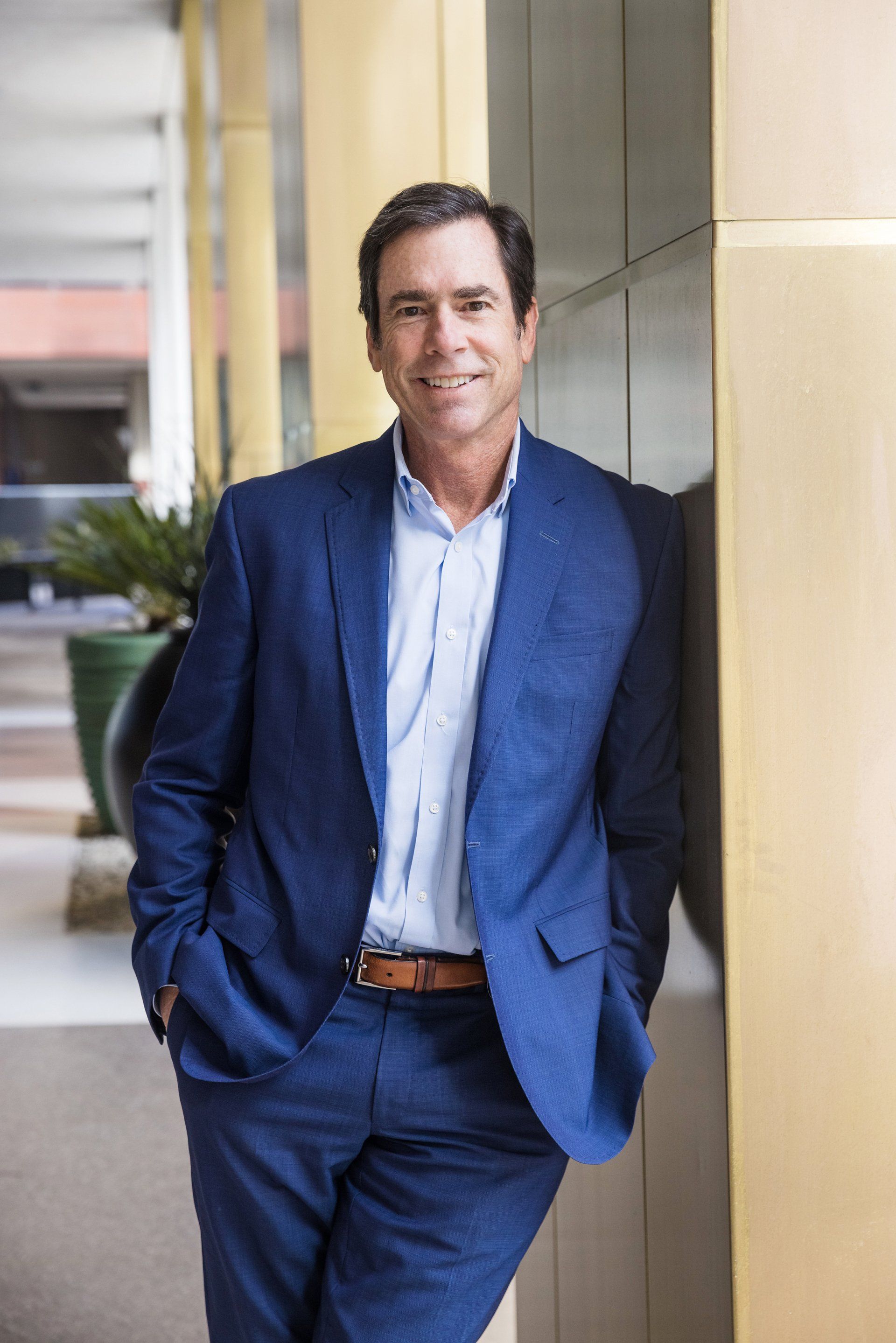 A man in a blue suit is leaning against a wall.