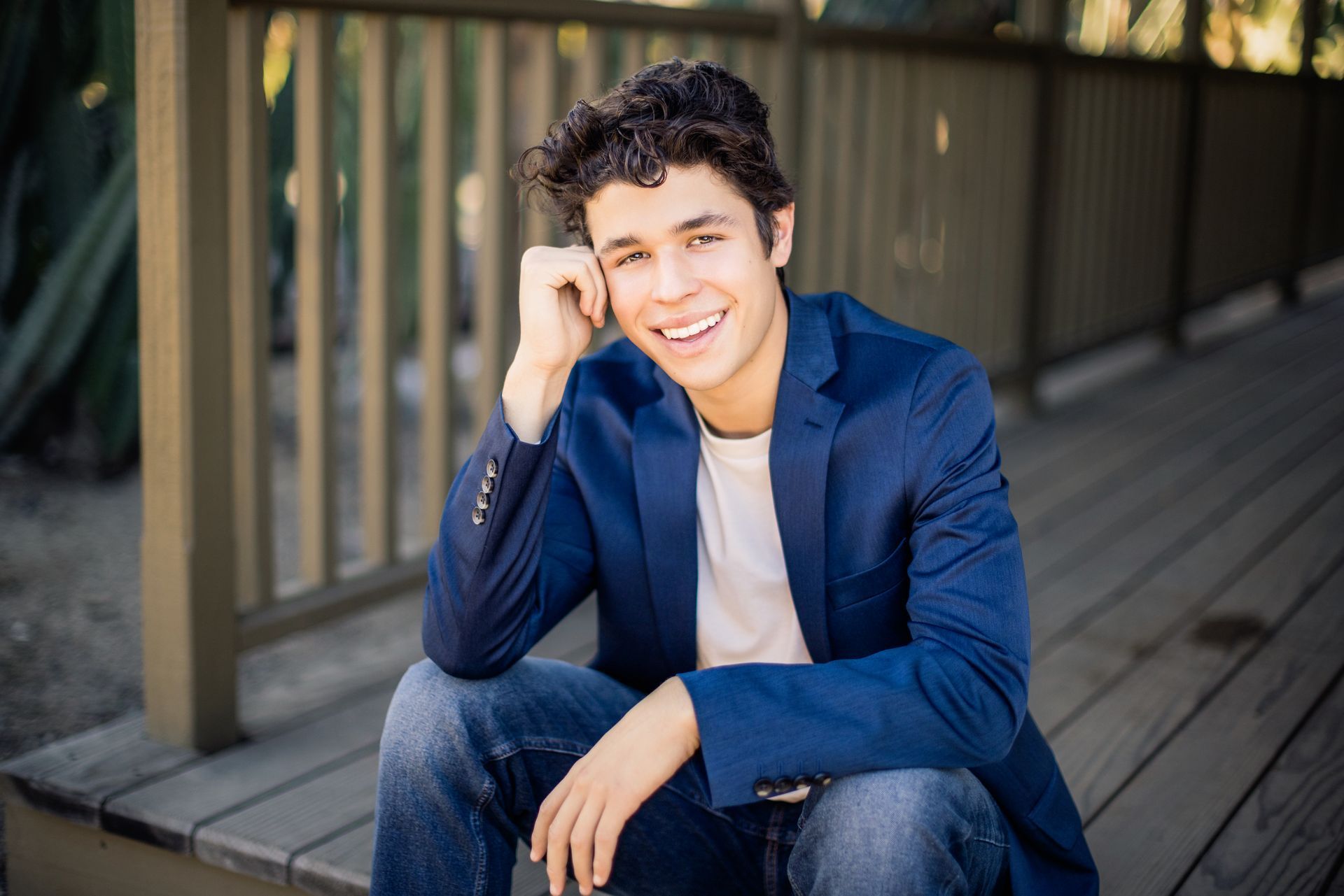 A young man in a blue jacket is sitting on a wooden deck.