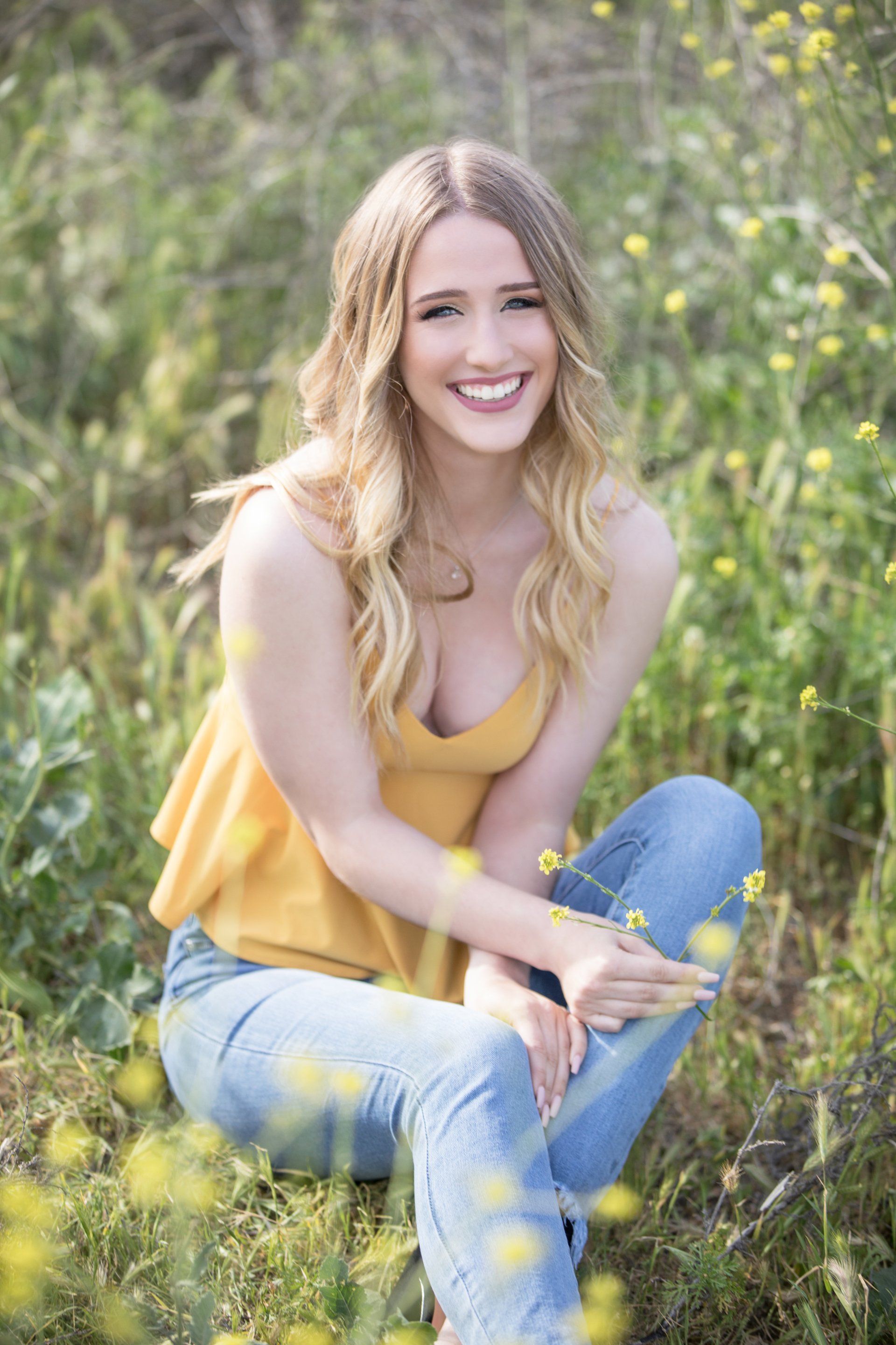 A young woman is sitting in a field of yellow flowers.