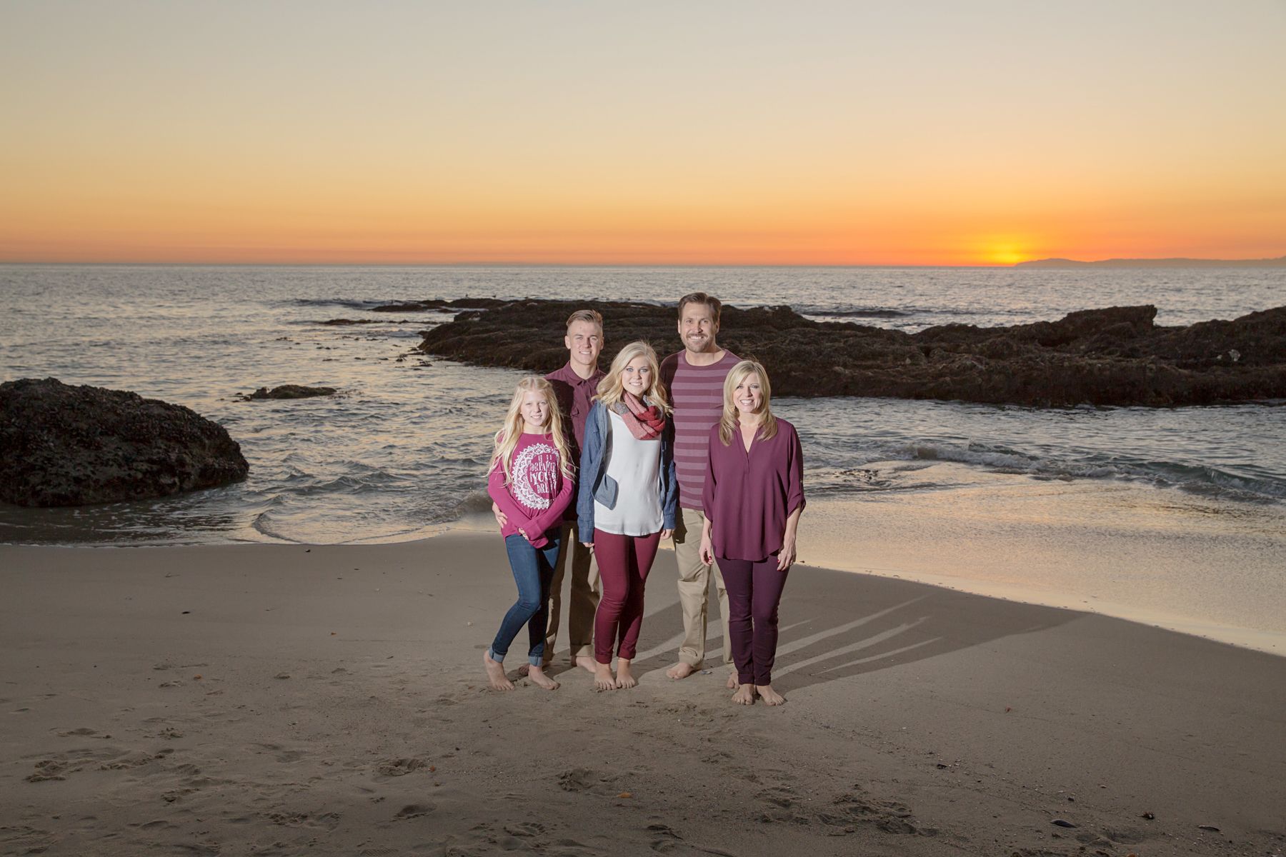 Family posing in front of the ocean while the sun is setting over Catalina at Victoria Beach