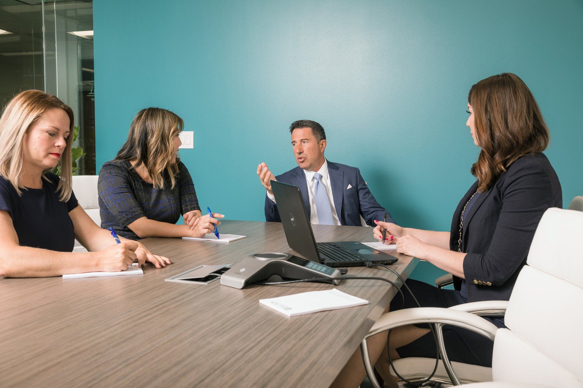A group of people are sitting around a conference table with a laptop.