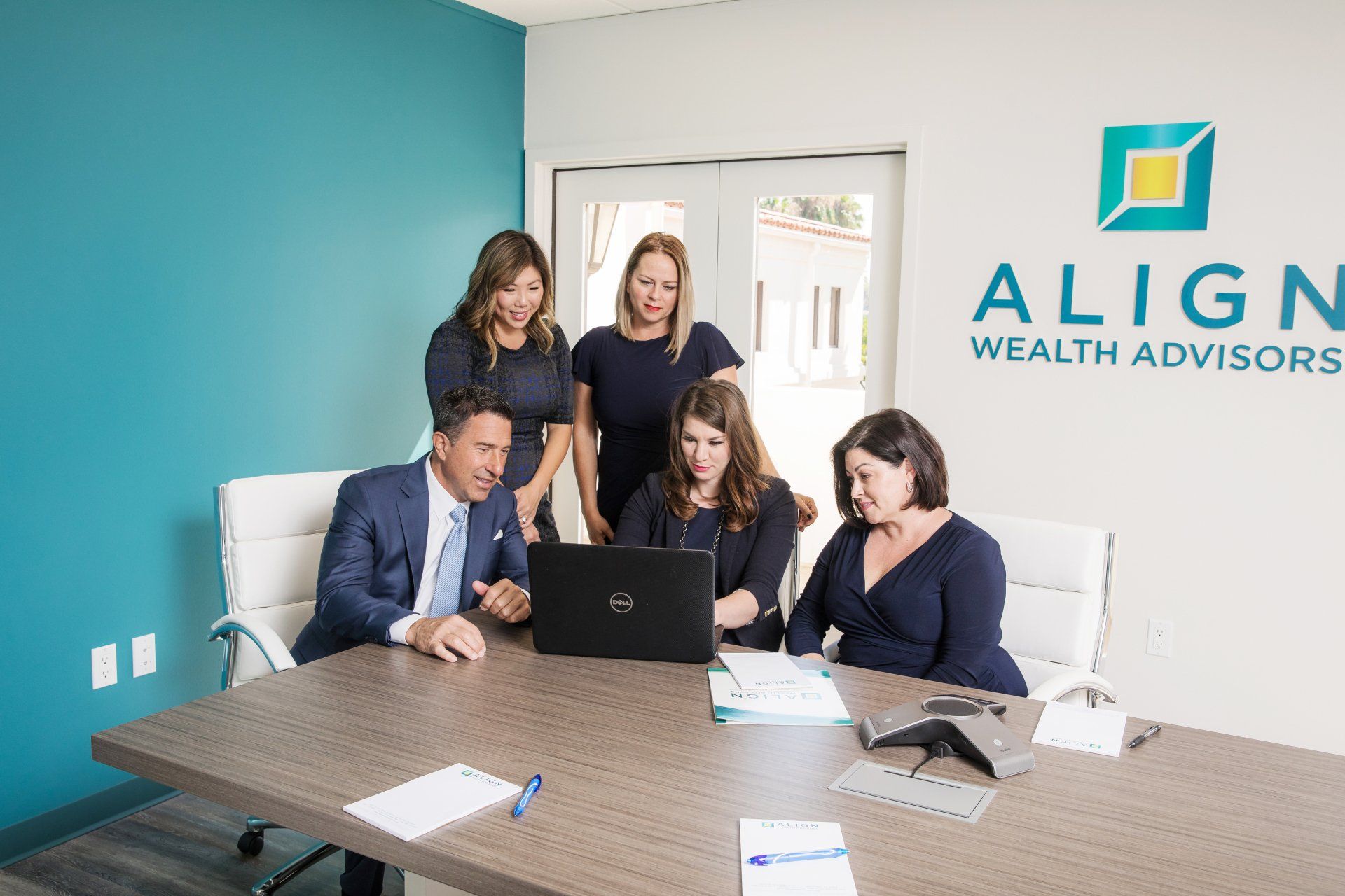 A group of people are sitting around a table looking at a laptop.