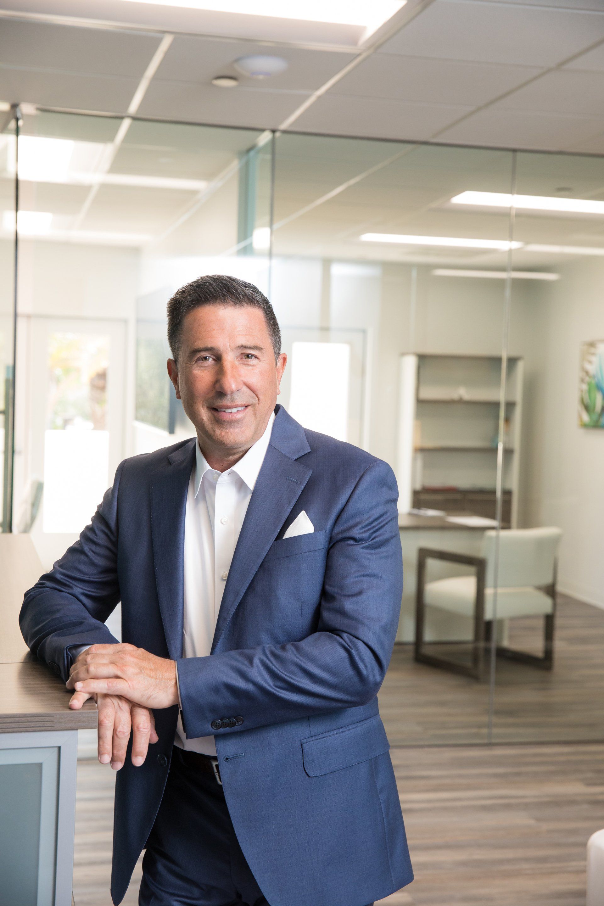 A man in a suit and tie is leaning on a counter in an office.