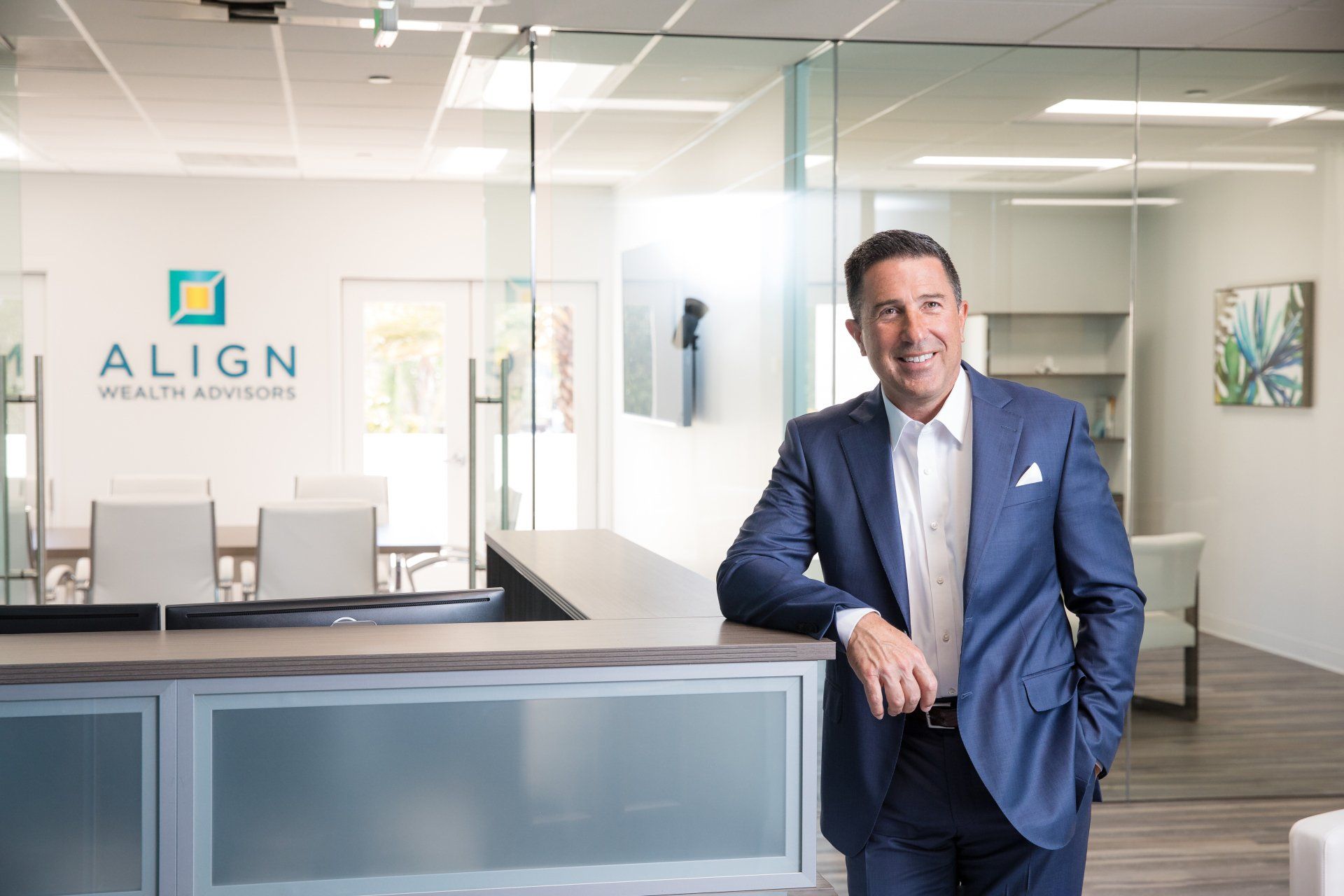 A man in a suit is leaning against a counter in an office.