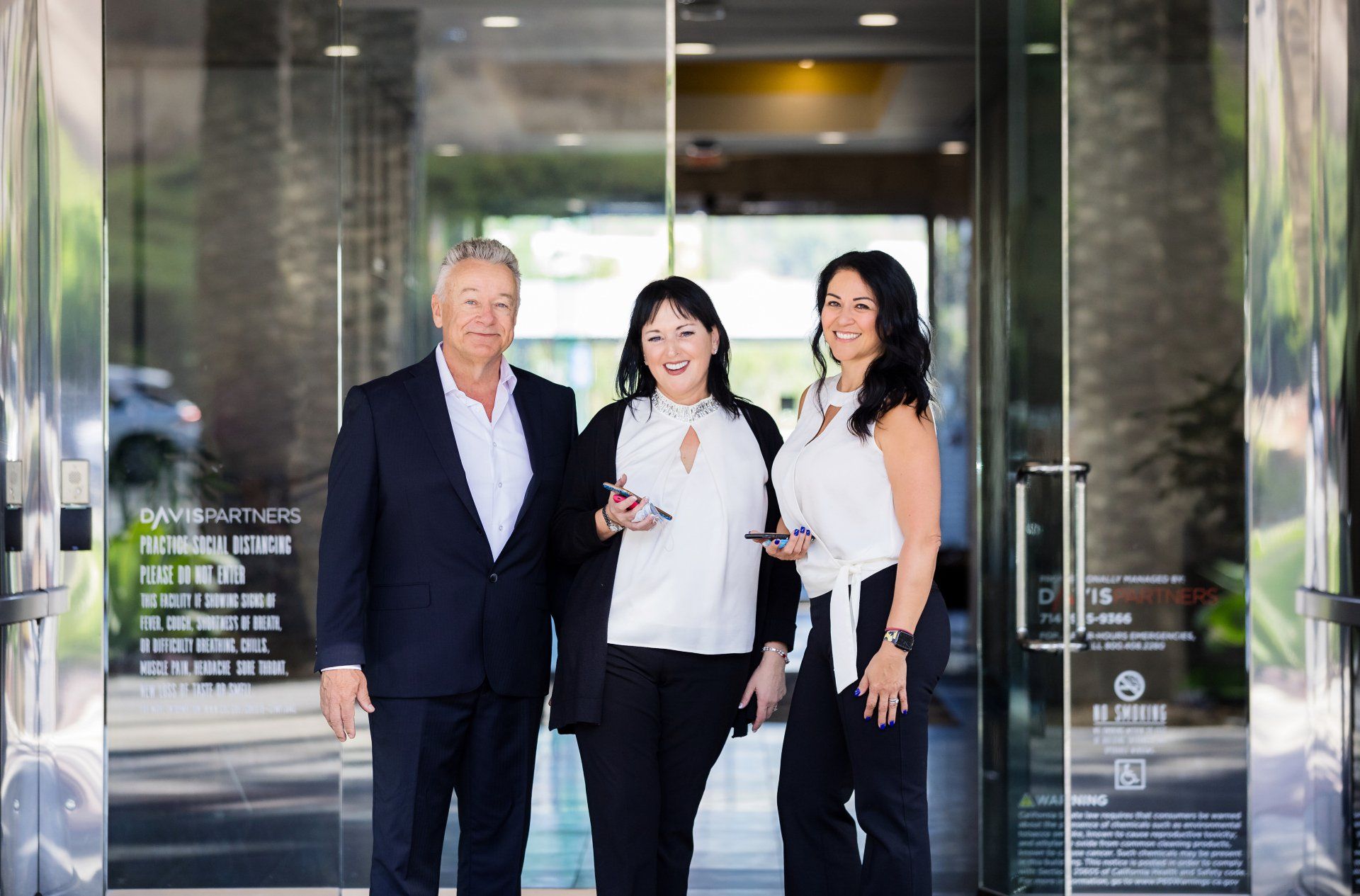 A man and two women are standing in front of a glass door.