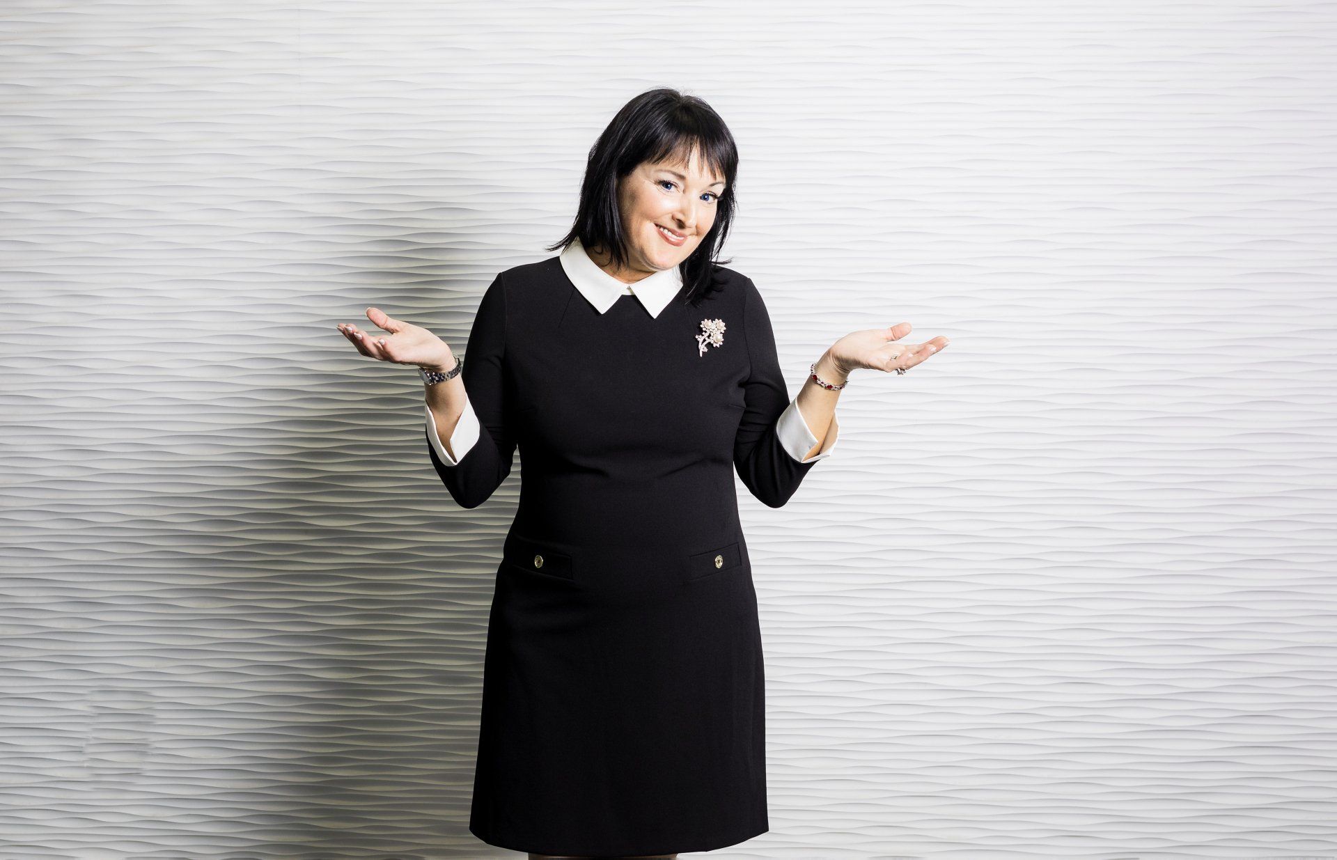 A woman in a black dress is standing in front of a white brick wall.