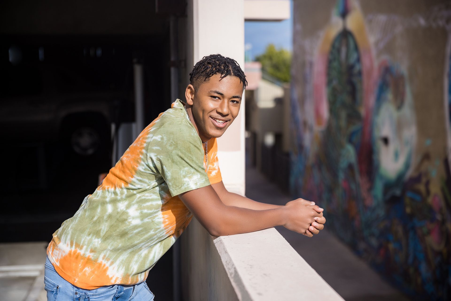 A young man leaning on a railing in front of a graffiti wall.