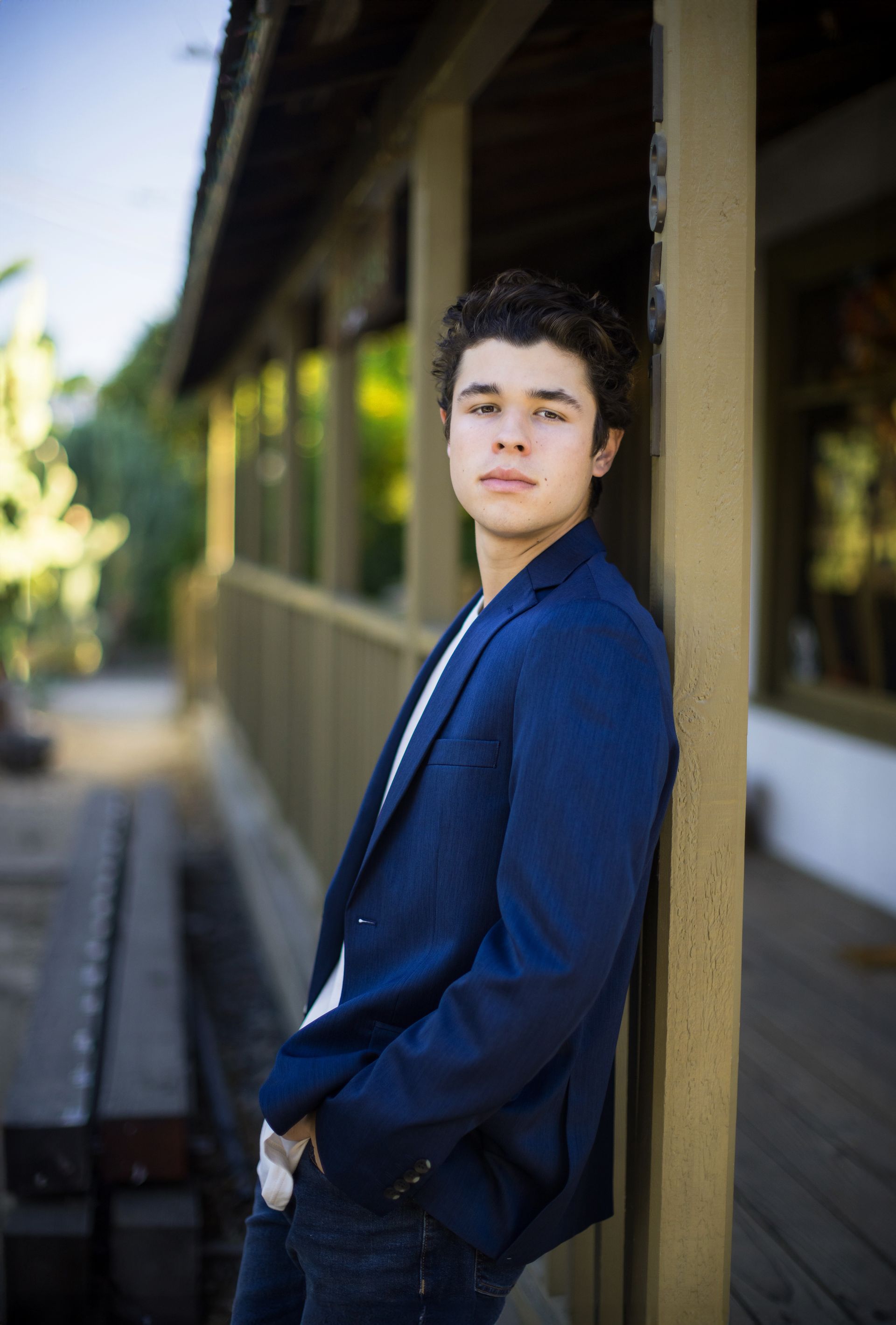 A young man in a blue jacket is leaning against a wooden post.