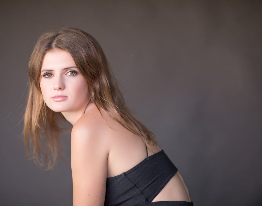 A woman in a black dress is sitting down and looking at the camera.