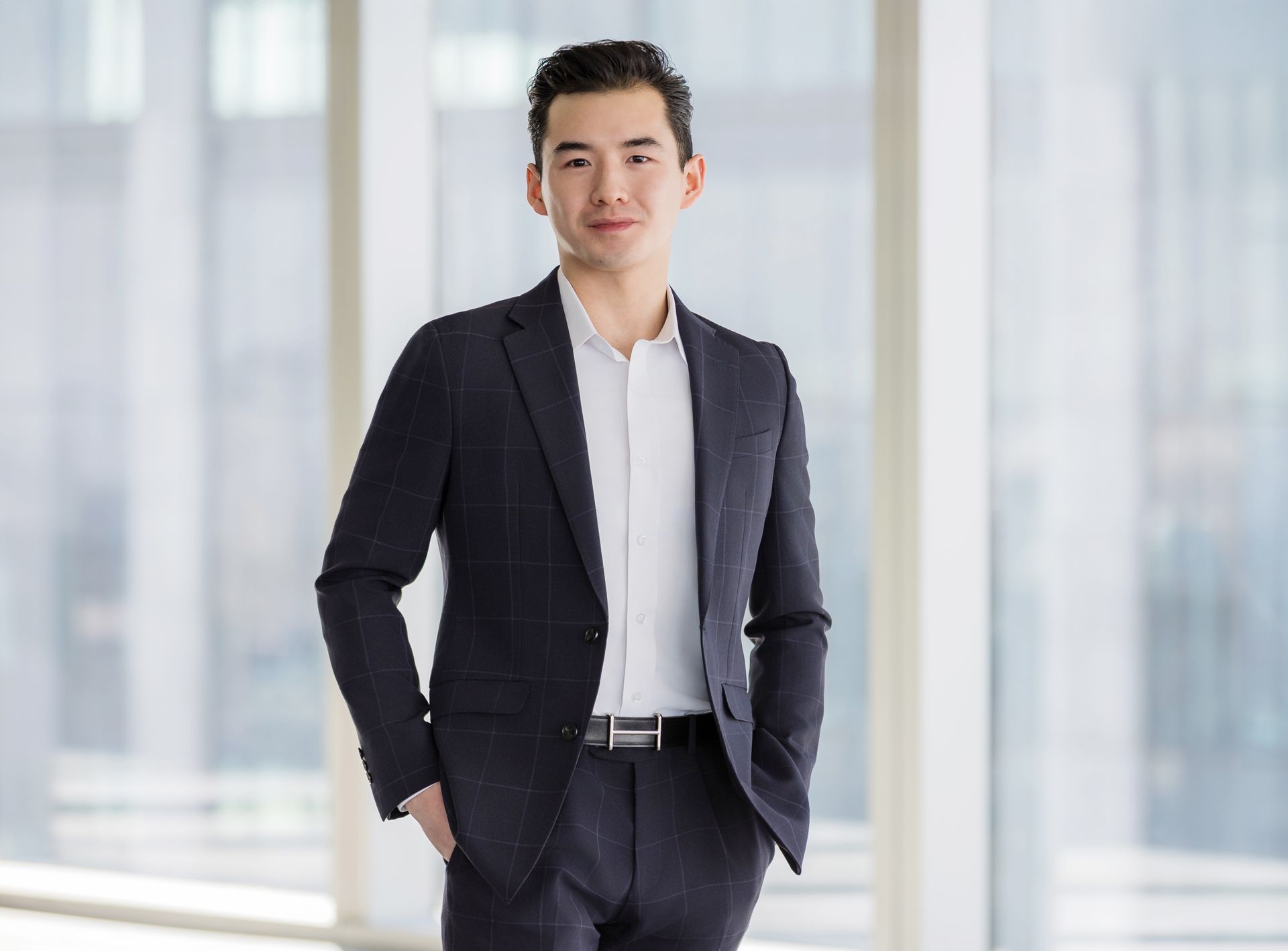A man in a suit and white shirt is standing in front of a window.