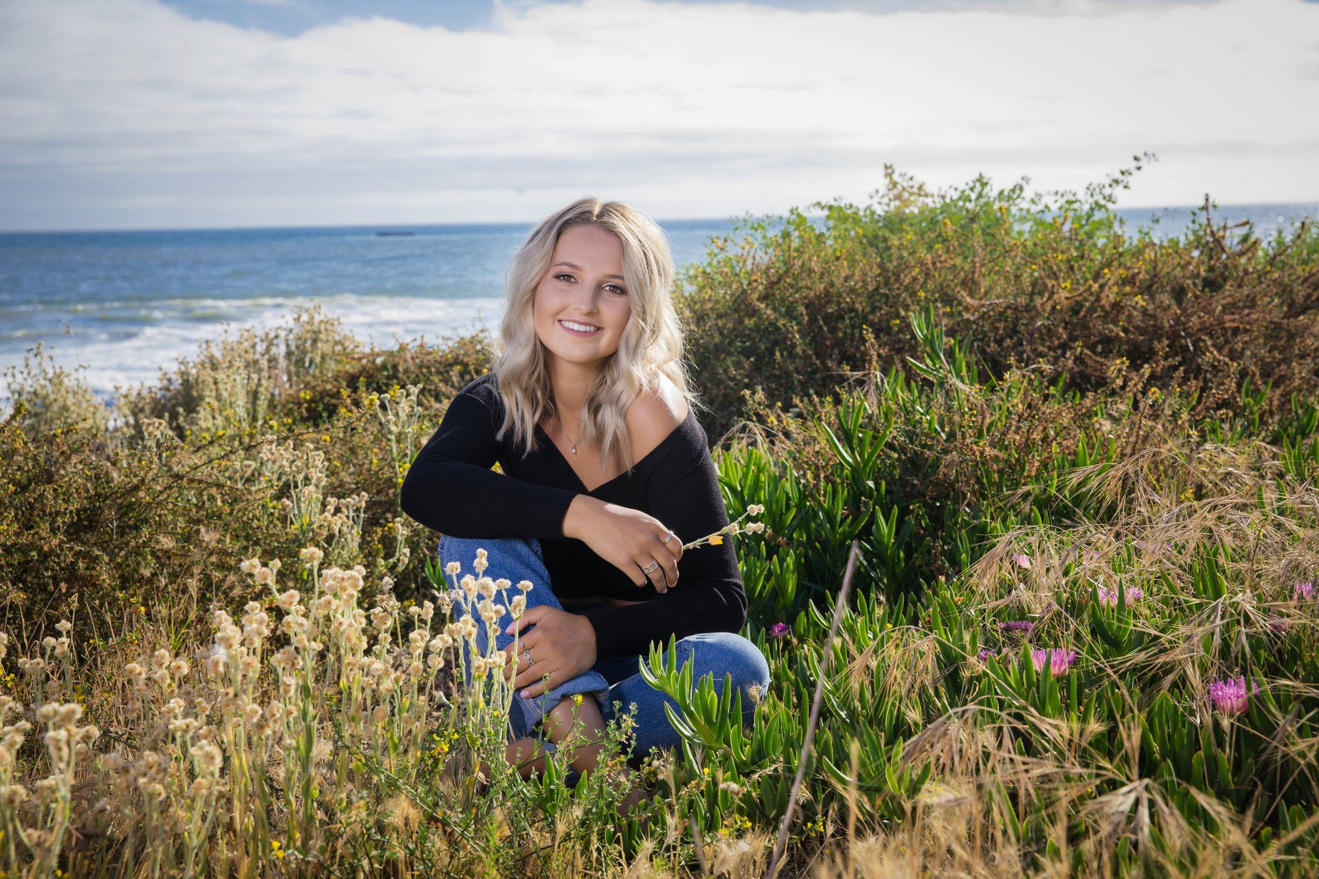 A woman is sitting in the grass near the ocean.