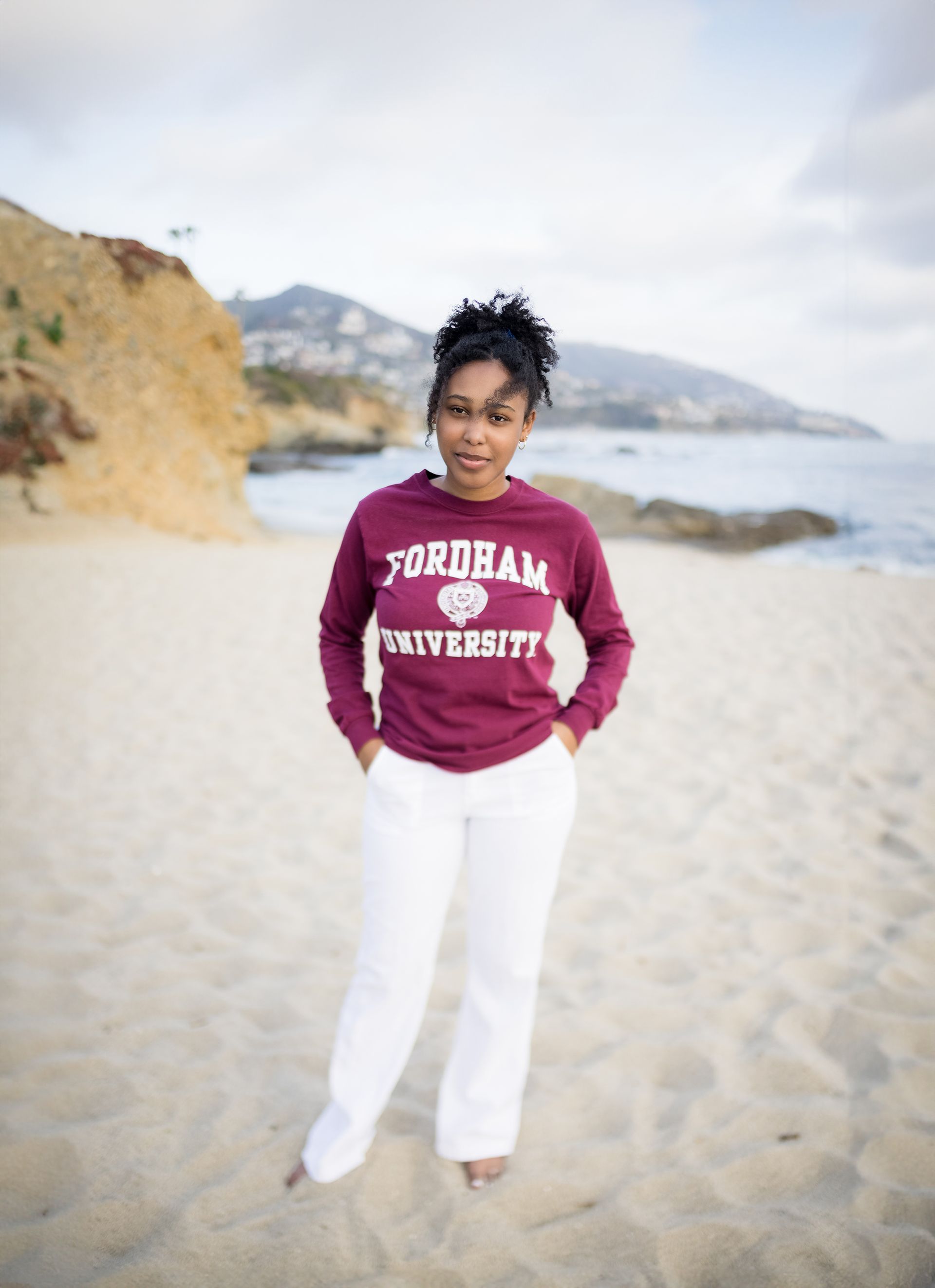 A woman is standing on a beach wearing a program university sweatshirt