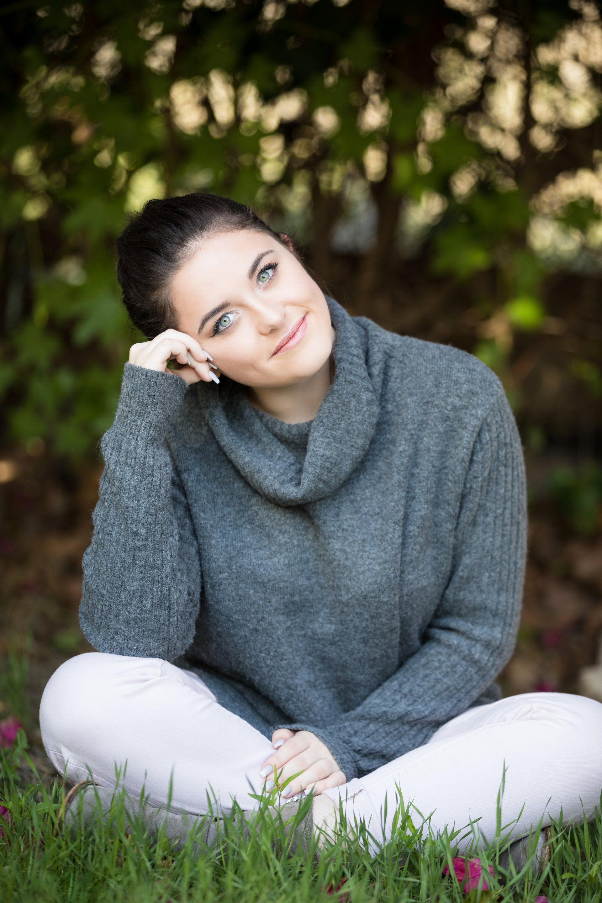A woman in a sweater is sitting on the grass with her legs crossed.