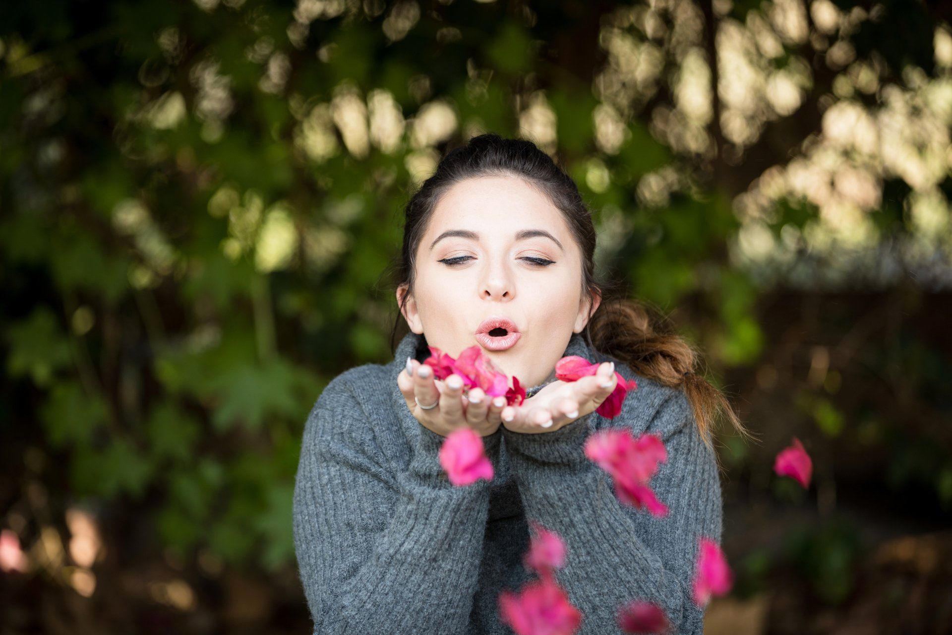 A woman is blowing pink flower petals out of her hands.