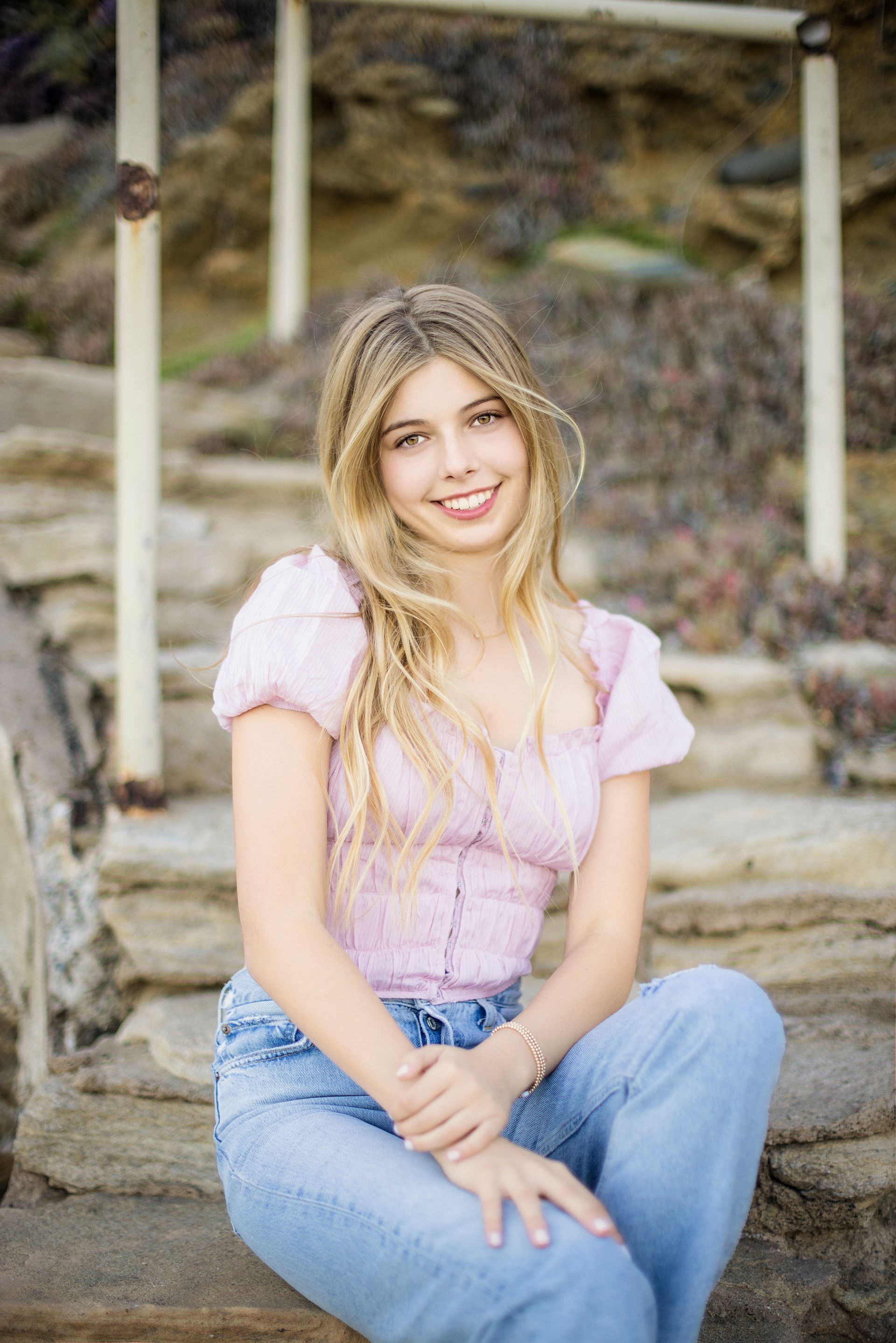 A young woman in a pink top and blue jeans is sitting on a set of stairs.