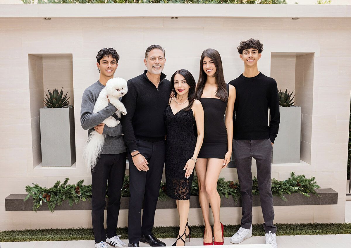 Lifestyle portrait of a family in their yard with their white poodle wearing black outfits and posing for a family portrait taken by Blue Sky's Studio at their Newport Beach residence.
