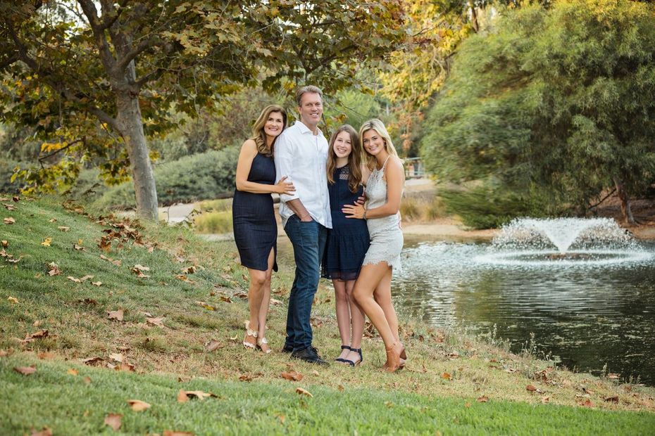 A family is posing for a picture in front of a pond in a park.