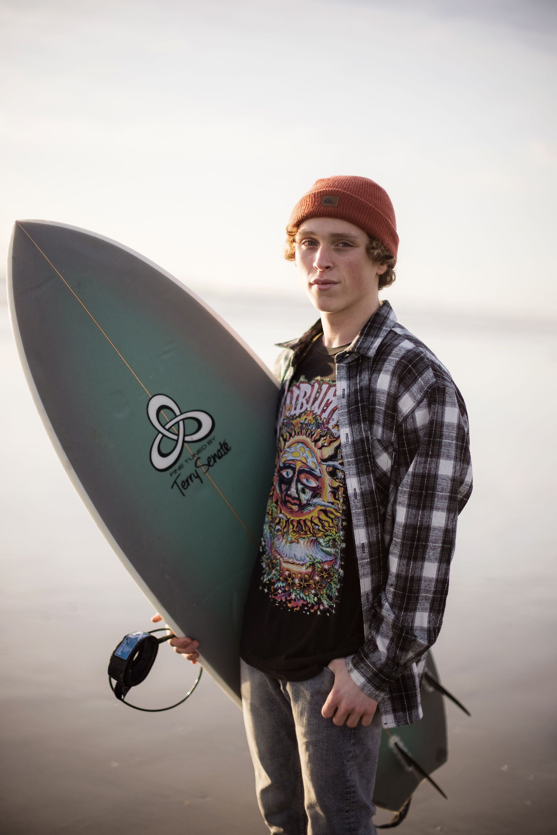 A young man is holding a surfboard on the beach.
