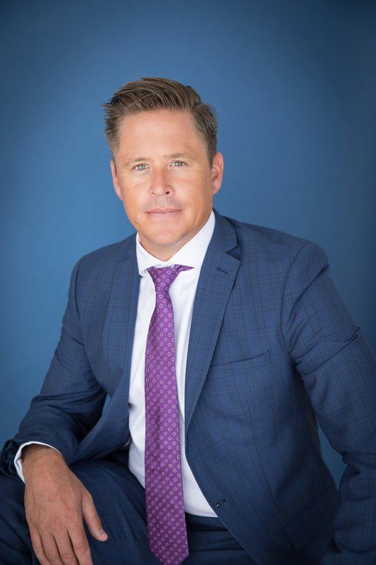 A man in a suit and tie is sitting in front of a blue background.