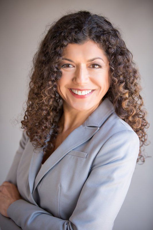 A woman with curly hair is wearing a suit and smiling.