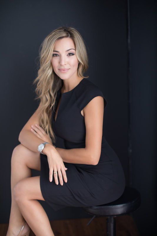 A woman in a black dress is sitting on a stool with her legs crossed.