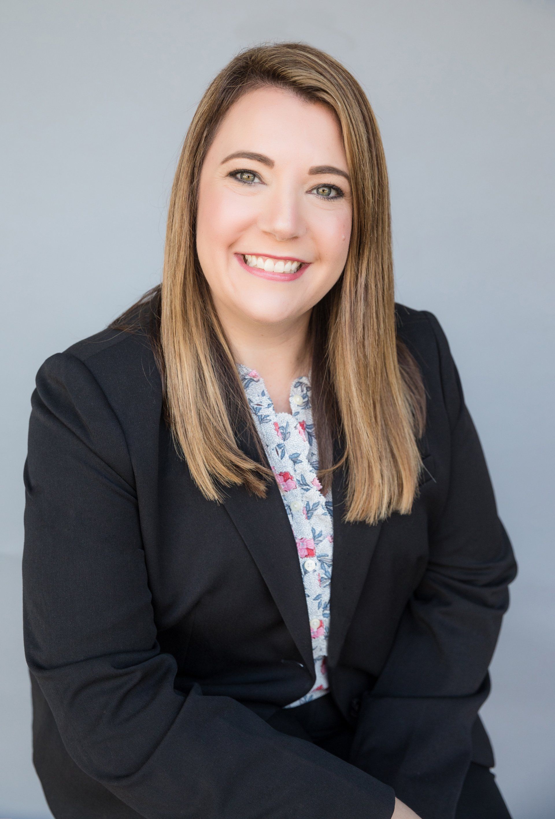 A woman in a suit and floral shirt is smiling for the camera.