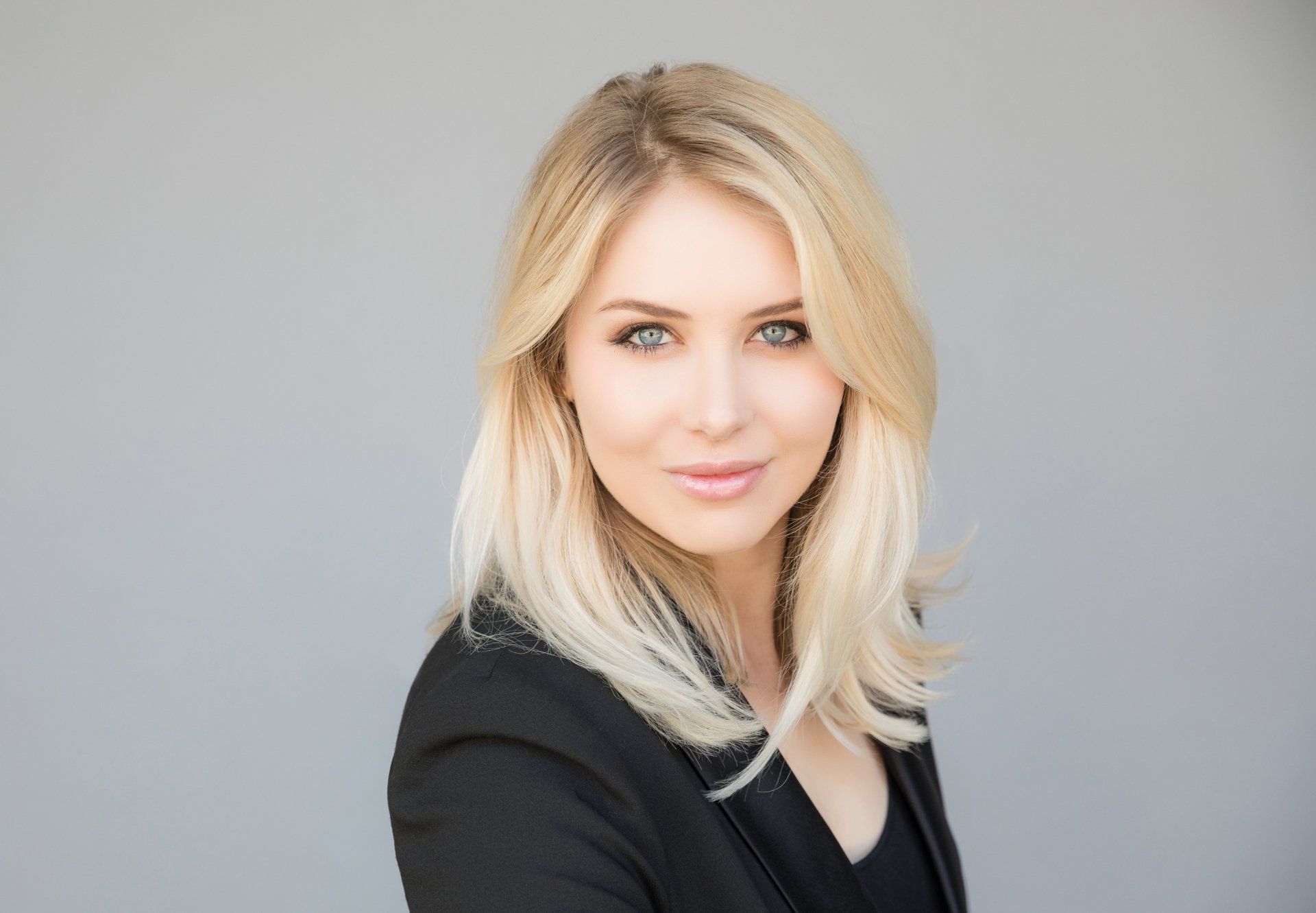 A woman with blonde hair is wearing a black jacket and looking at the camera.