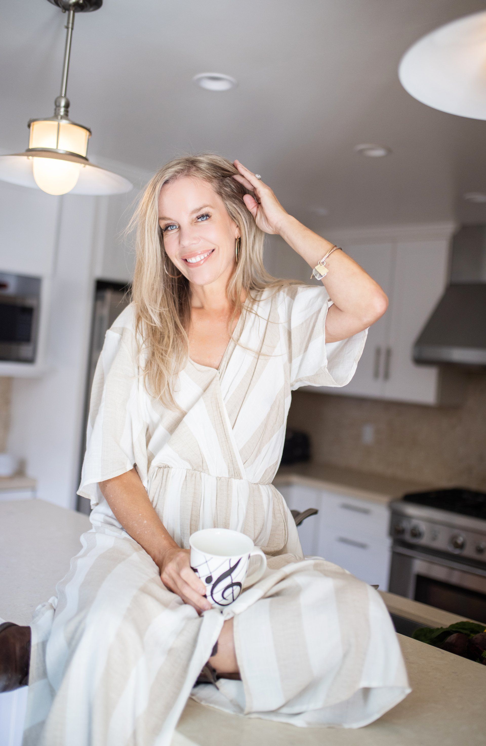 A woman is sitting on a counter in a kitchen holding a cup of coffee.