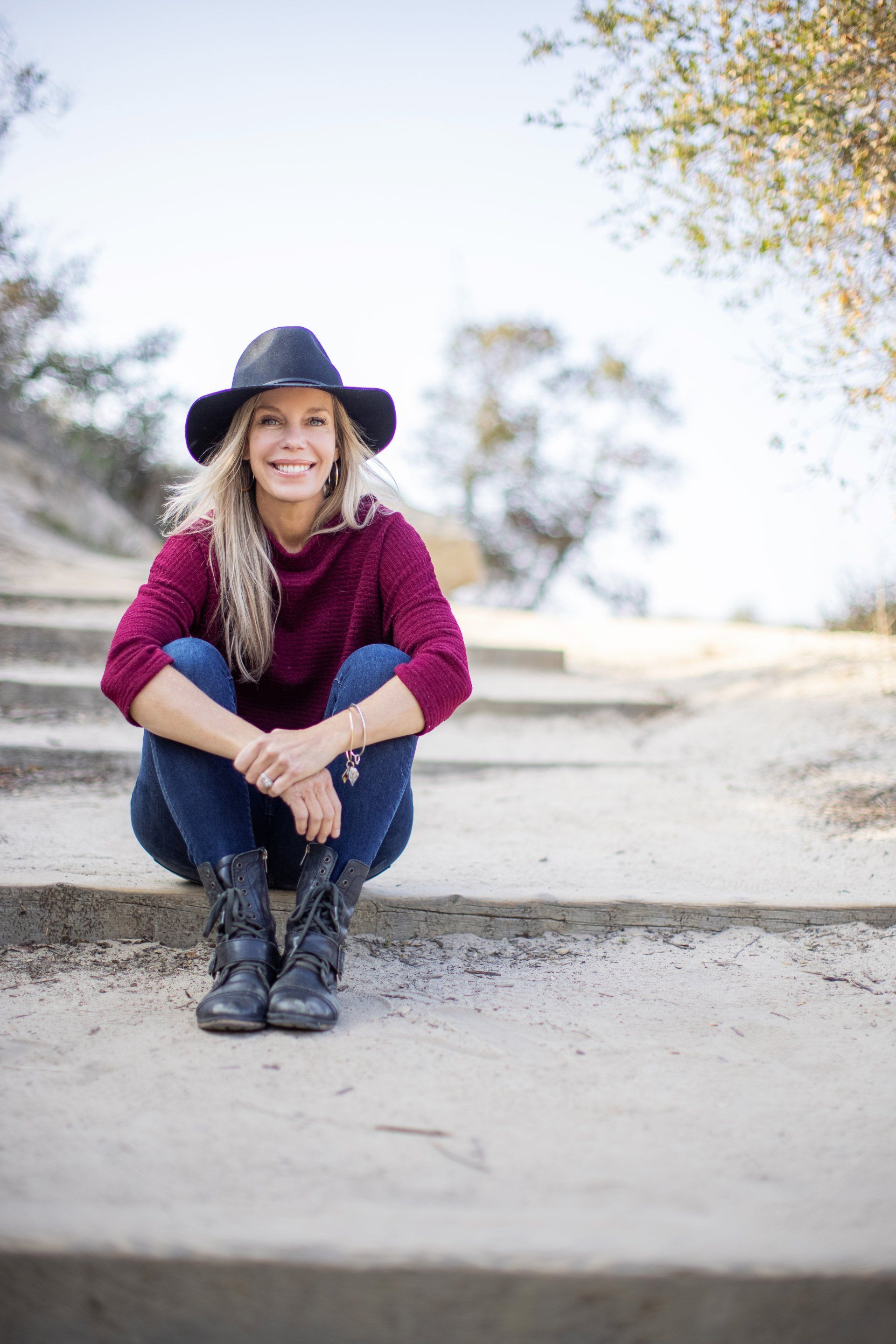 A woman wearing a hat and a sweater is squatting down on a set of stairs.