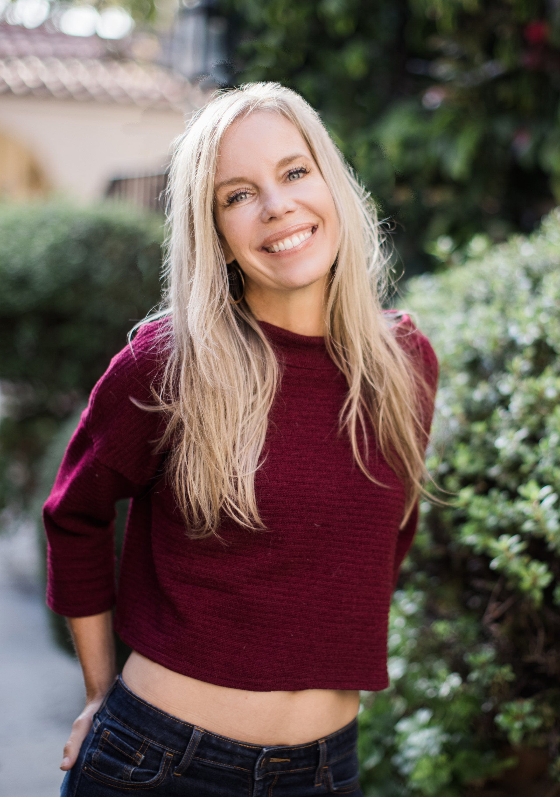 A woman wearing a burgundy crop top and jeans is smiling for the camera.