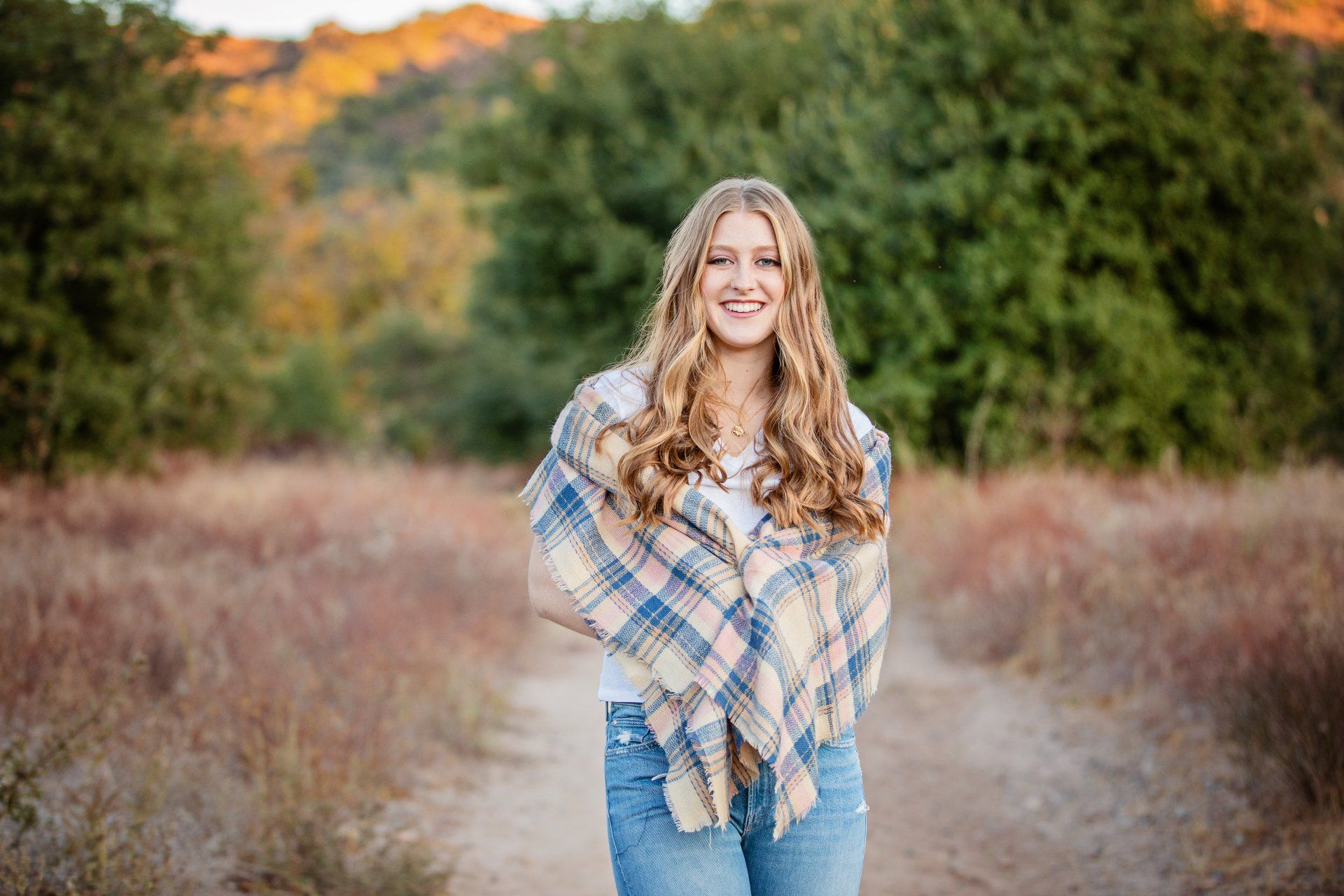 A young woman wearing a plaid scarf is standing in a field.