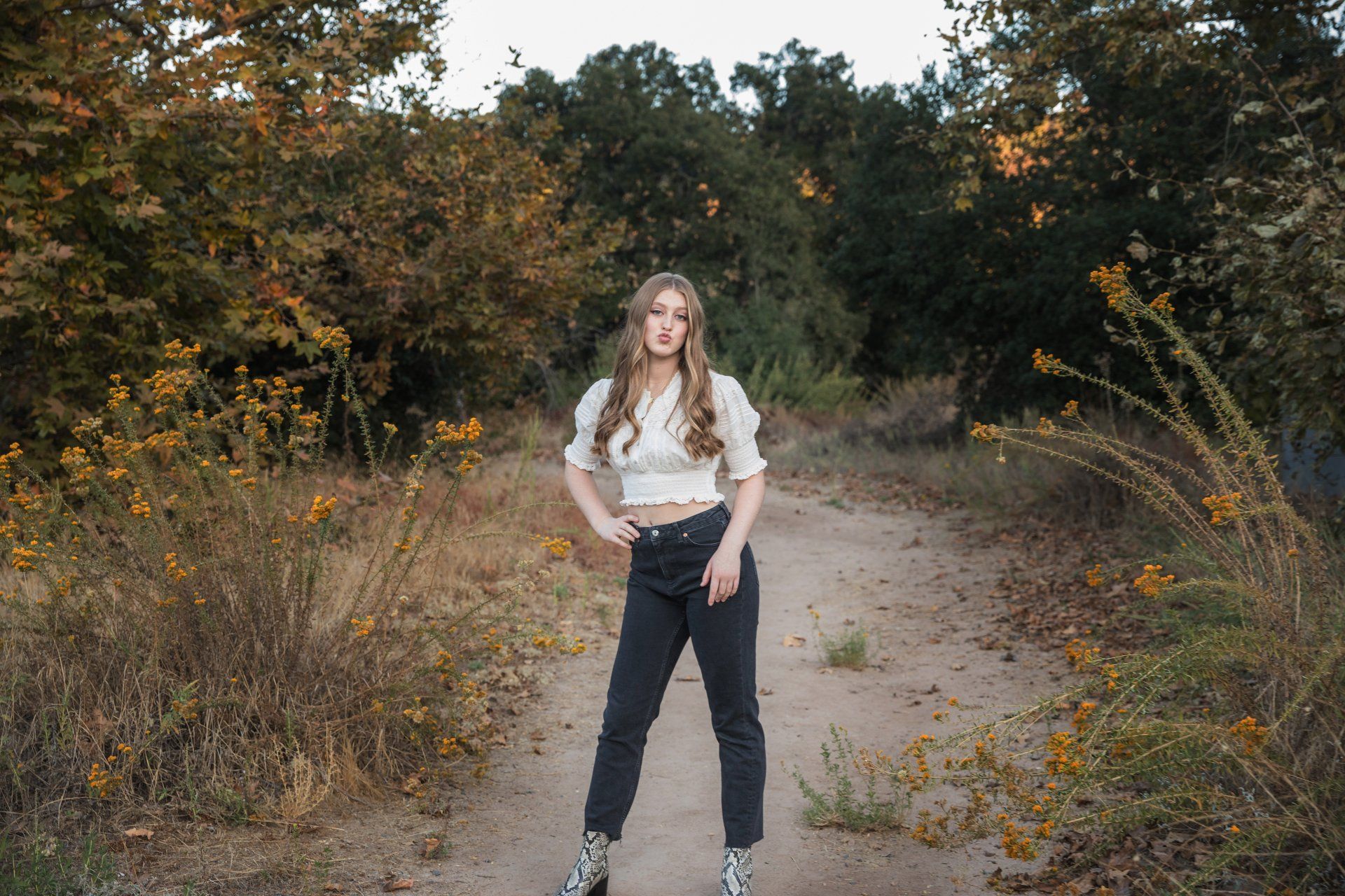 A woman is standing on a dirt road in the woods.