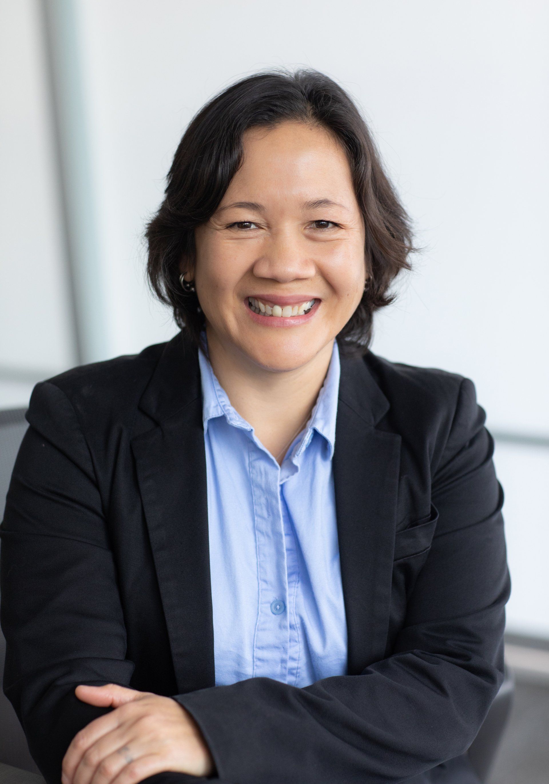 A woman in a suit and blue shirt is smiling with her arms crossed.