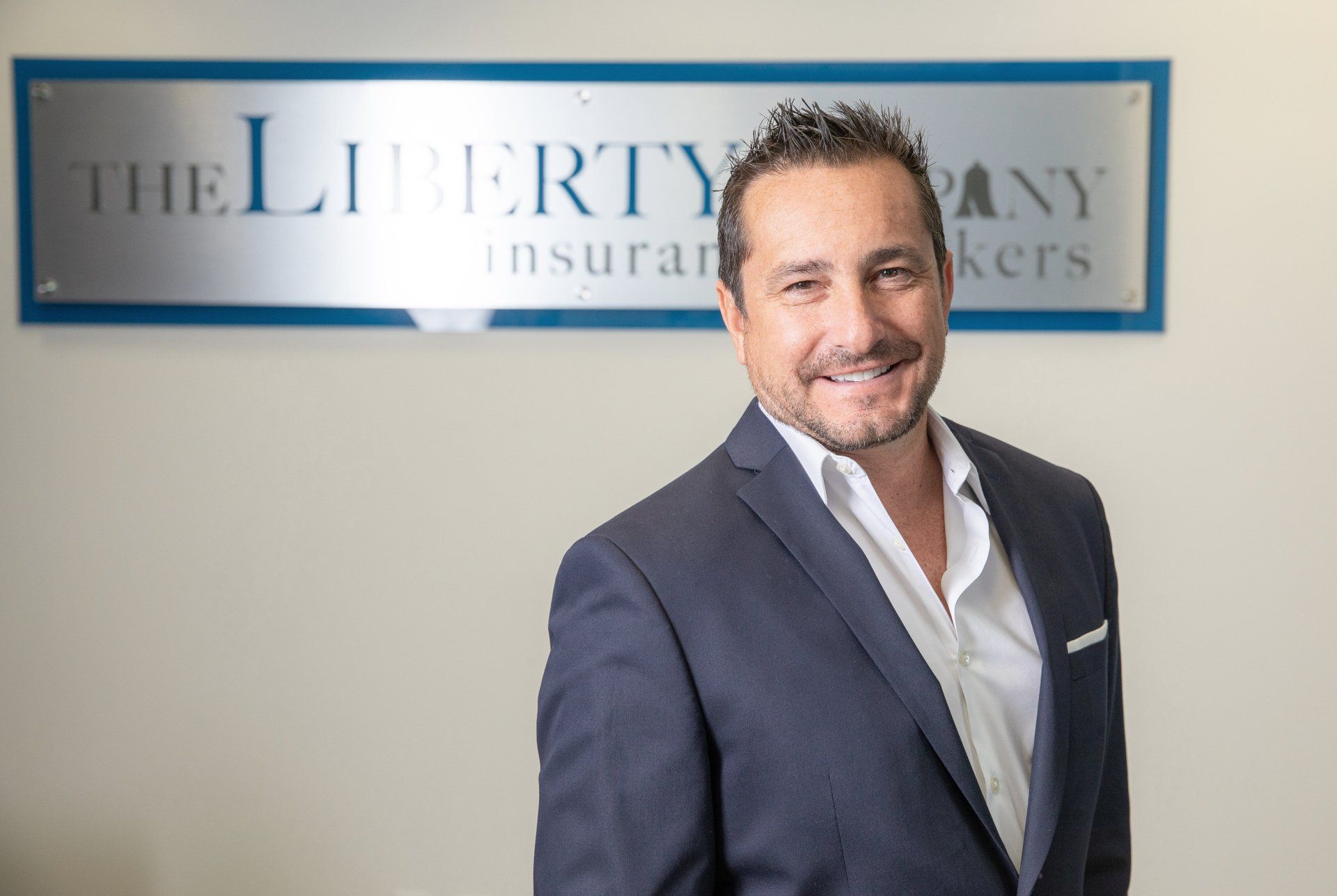 A man in a suit is standing in front of a sign for the liberty insurance company.