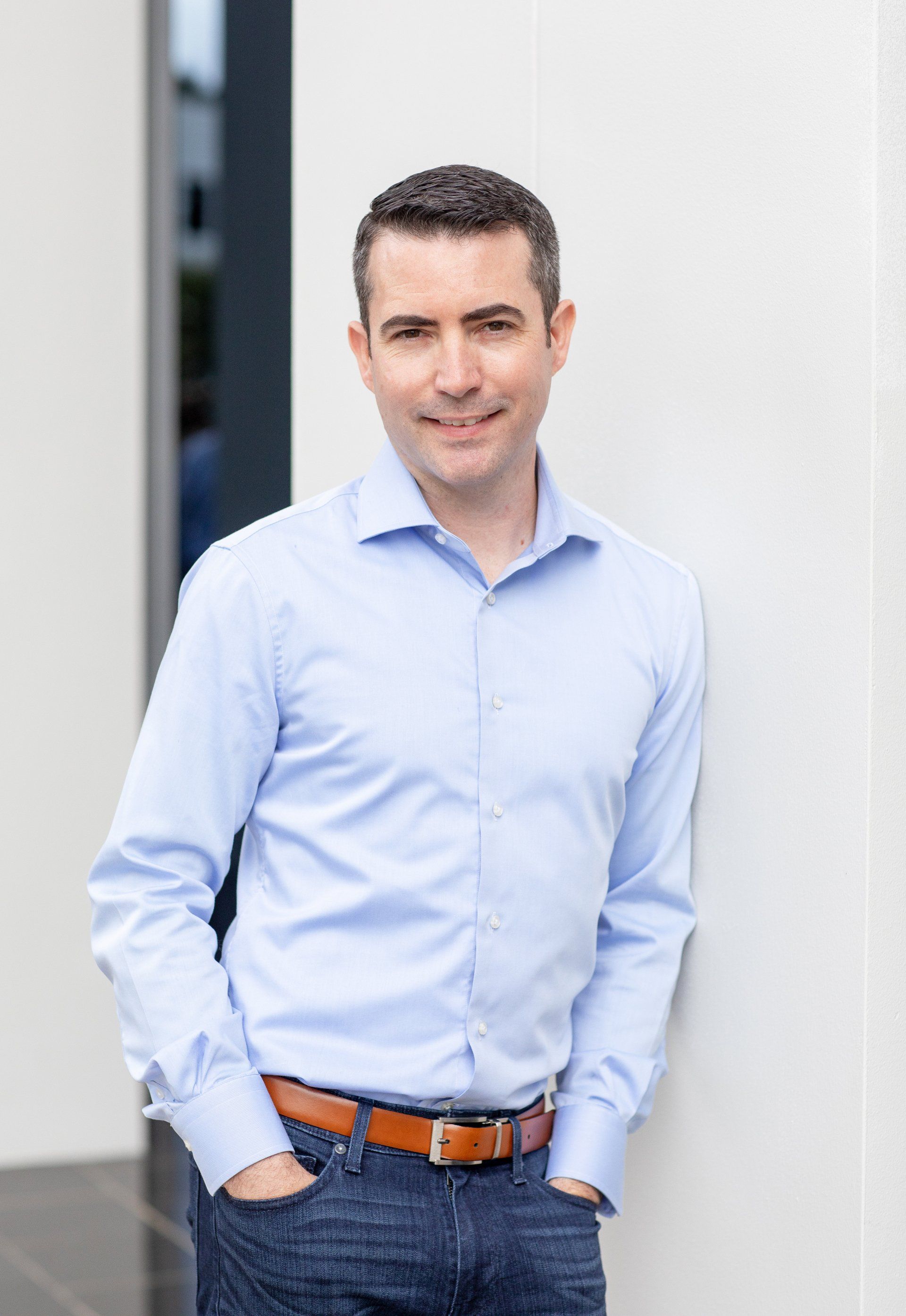 A man in a blue shirt and jeans is leaning against a wall.
