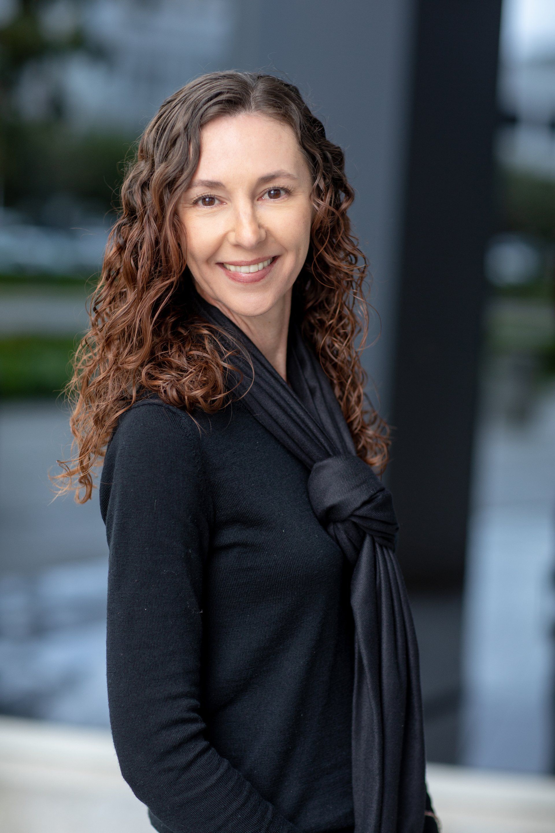 A woman wearing a black sweater and scarf is smiling for the camera.
