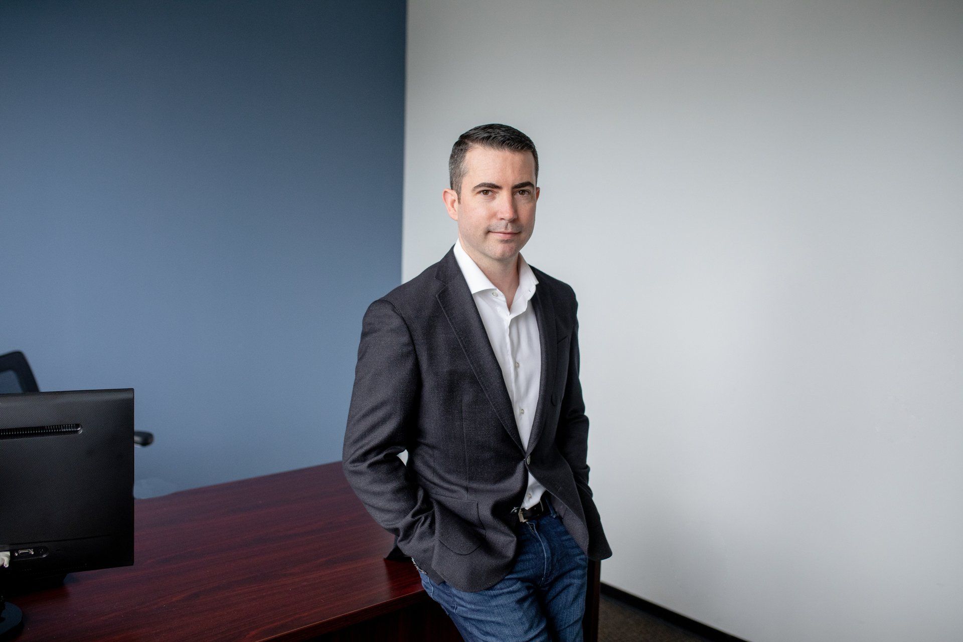 A man in a suit is sitting at a desk with his hands in his pockets.