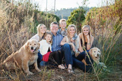 A family is posing for a picture in a field with their dogs.