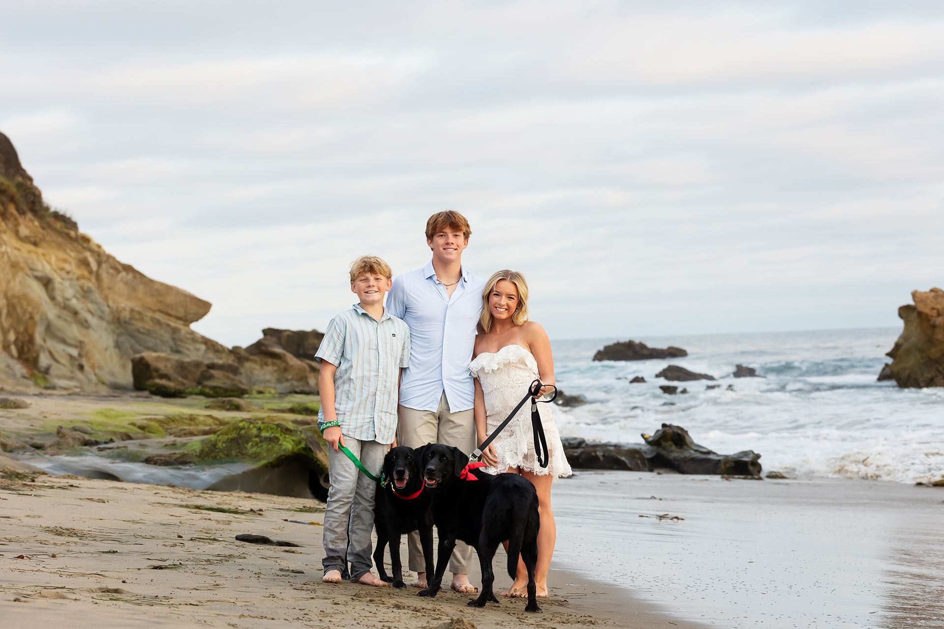 Siblings with their dogs posing at the beach during a family photo session in Laguna Beach.