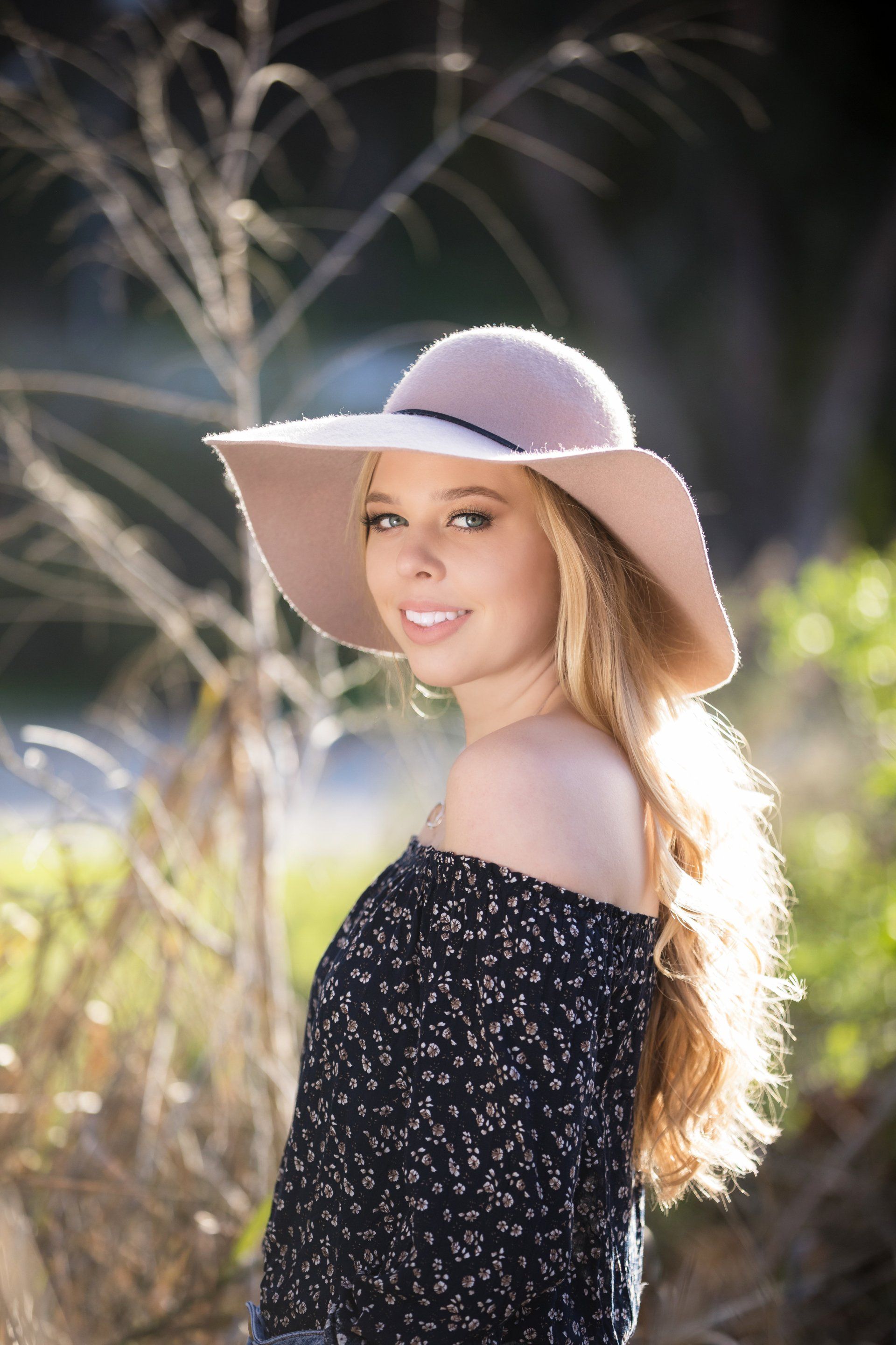 A woman wearing a hat and a black off the shoulder top is standing in a field.