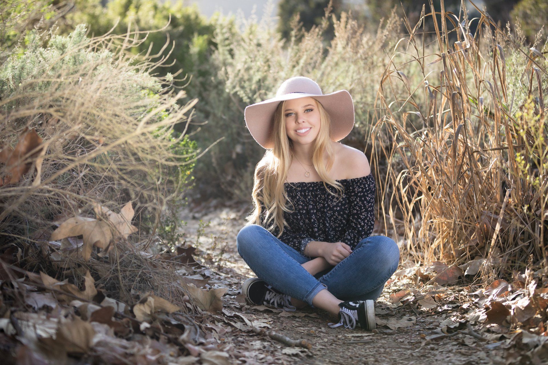 A woman wearing a hat is sitting on the ground in a field.