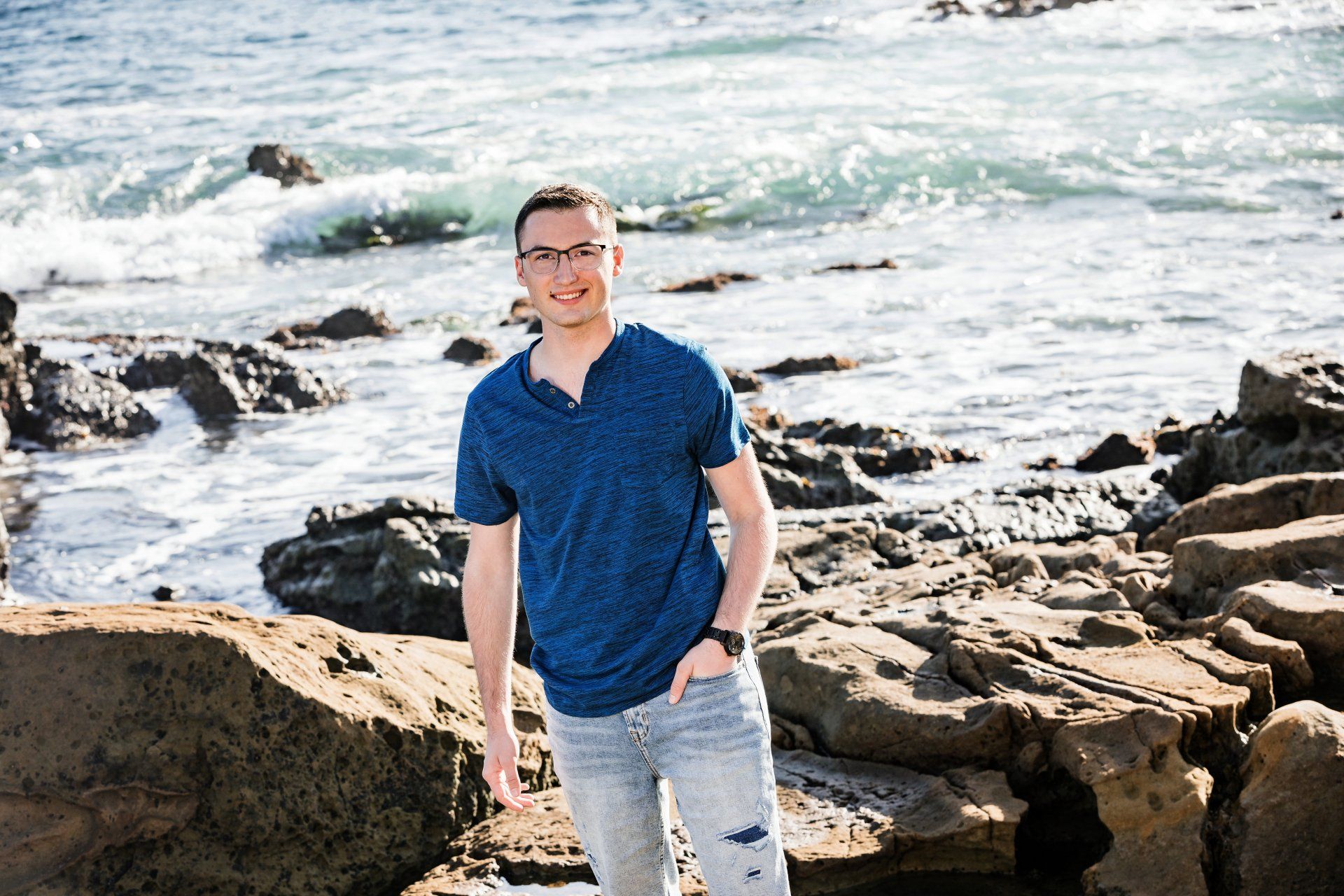 A young man is standing on a rocky beach near the ocean.