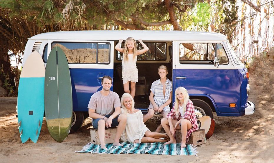 A family is sitting in the back of a blue van with surfboards.