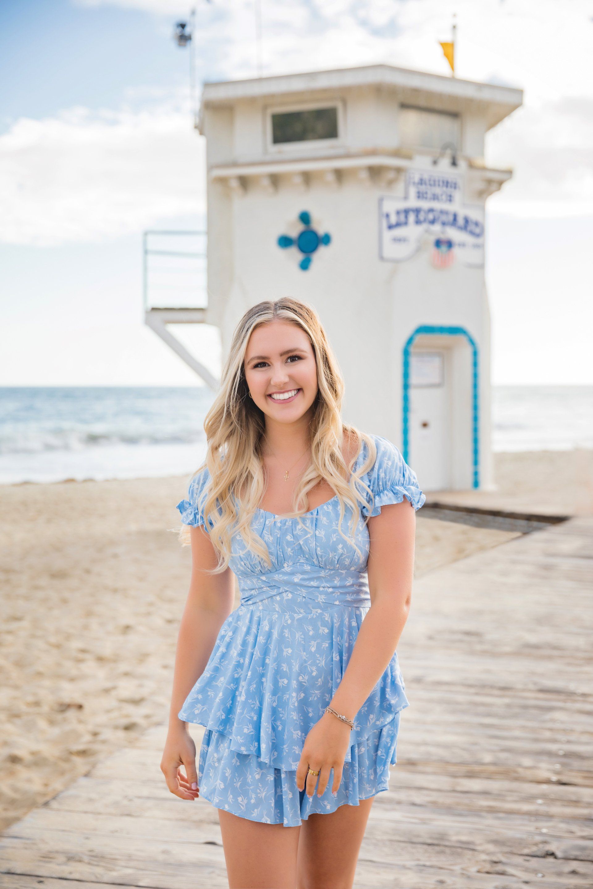 A woman in a blue dress is standing in front of a lifeguard tower on the beach.