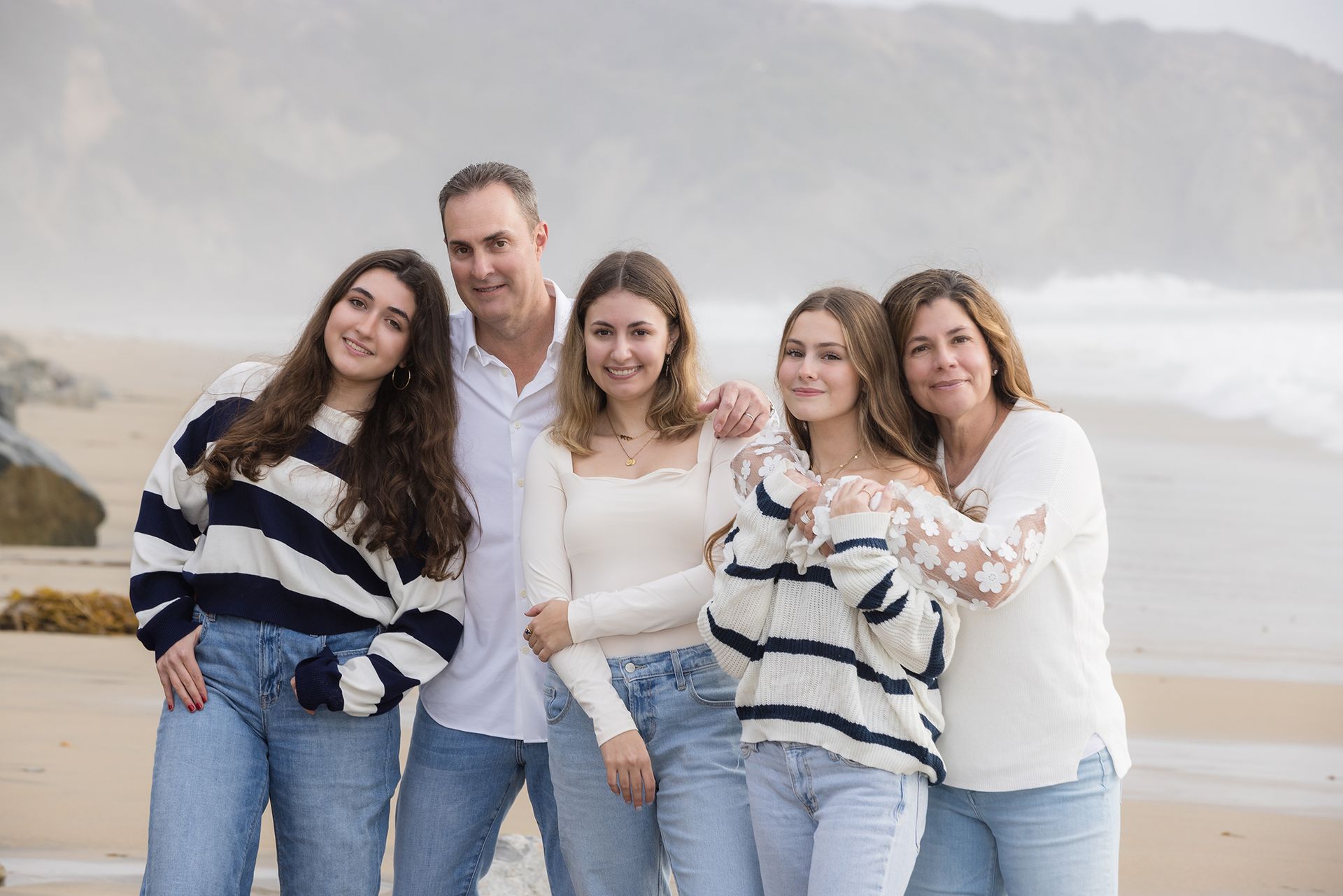 Family of five posing on a misty beach snuggling close together.