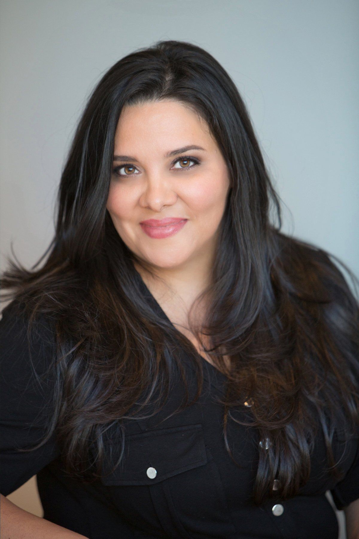 A woman with long dark hair is wearing a black shirt and smiling for the camera.