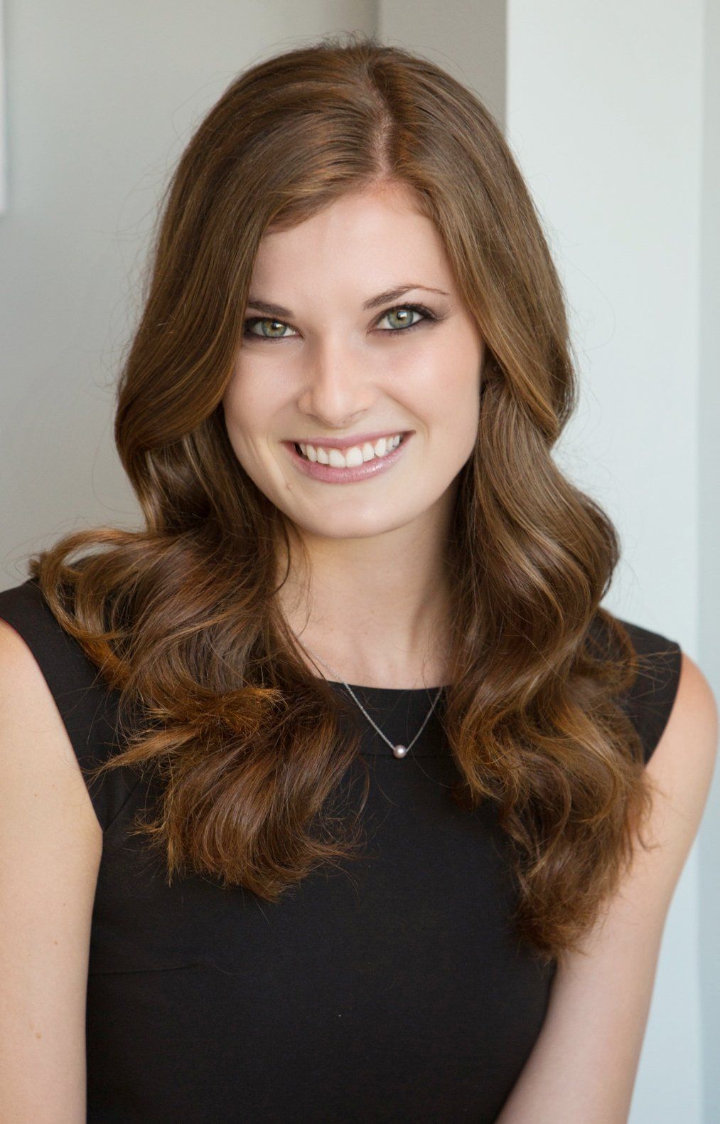 A woman in a black dress and necklace is smiling for the camera.