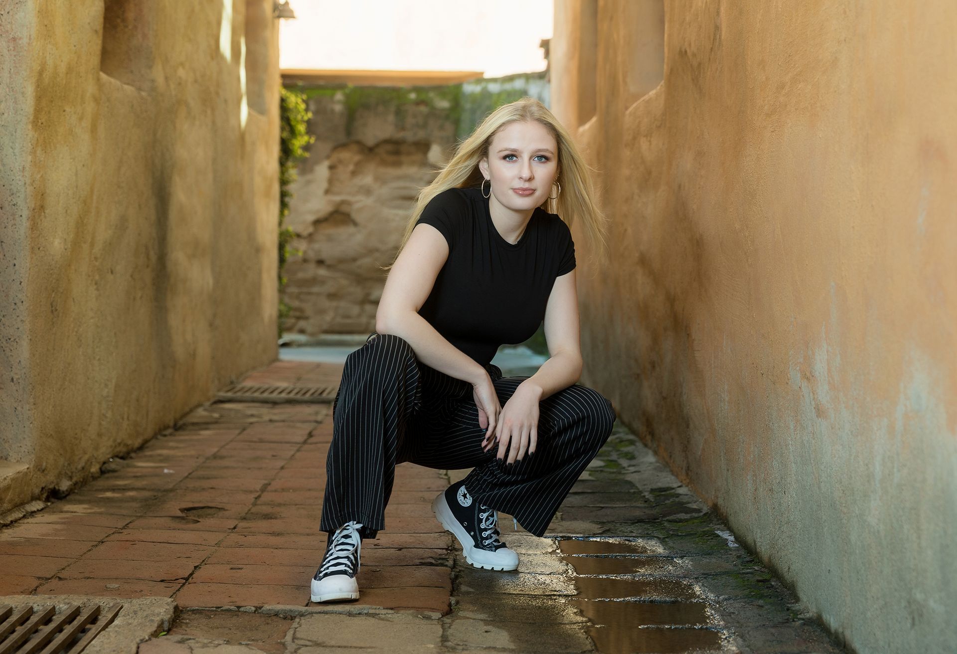 A woman is squatting down in a narrow alleyway.